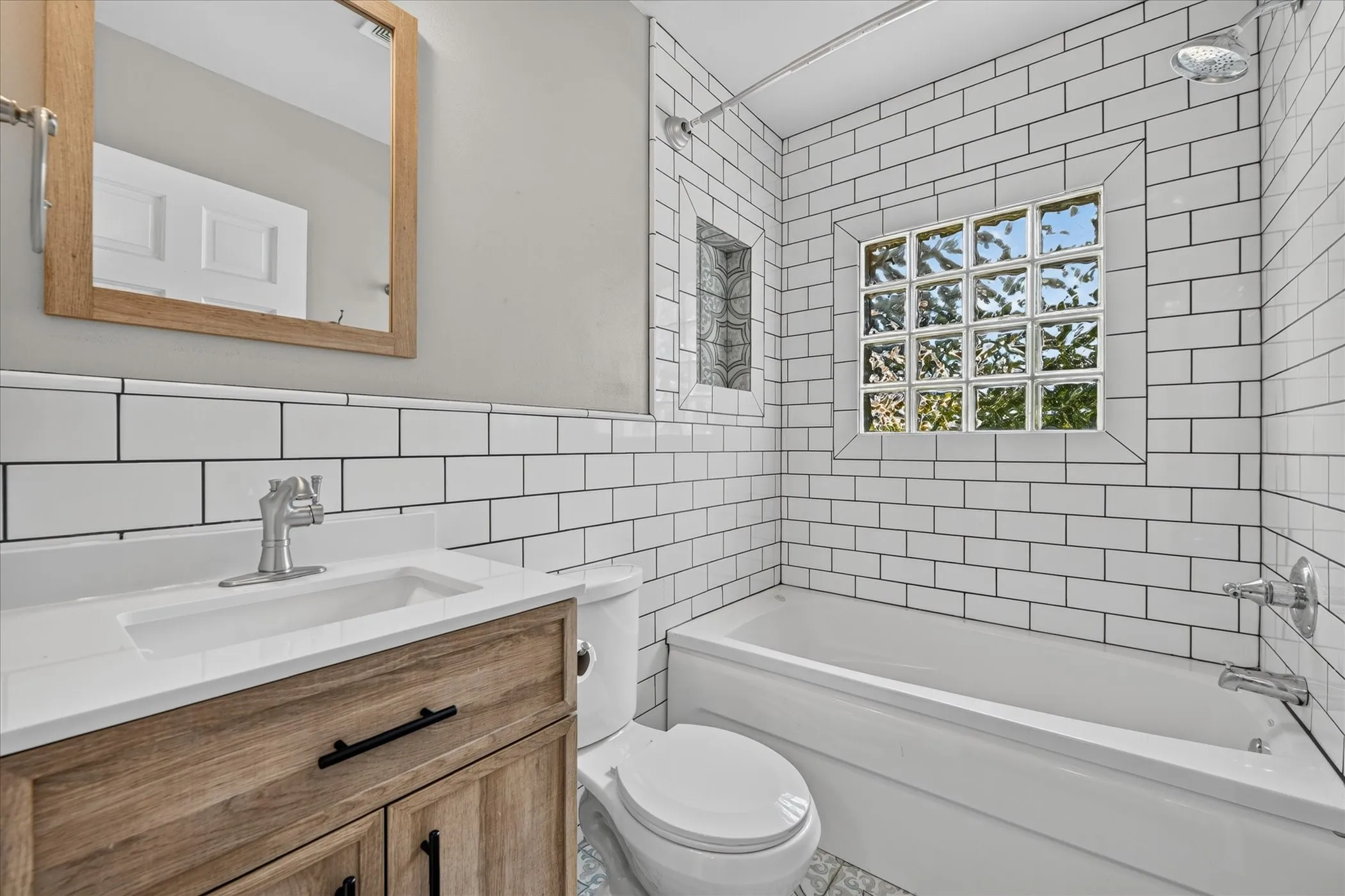 Built-in bathtub with subway tile surround, glass block window, recessed niche, wood-finish vanity, and integrated sink