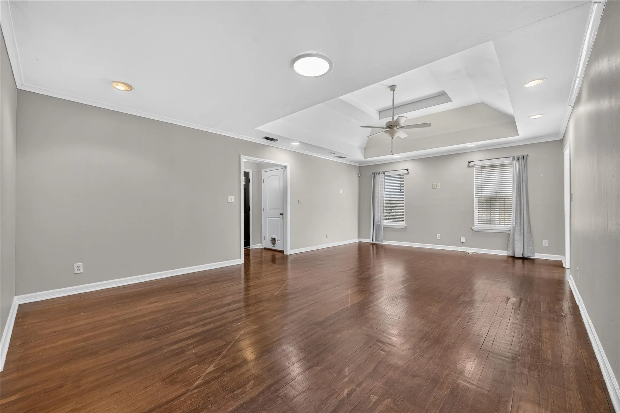 Wood-finish flooring, tray ceiling, recessed lighting, ceiling fan, and crown molding