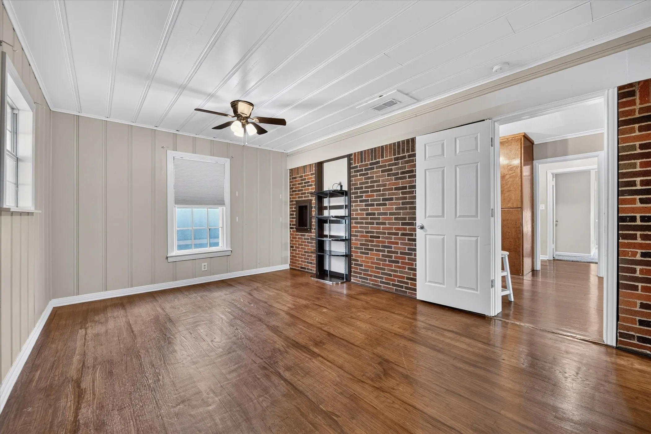 Wood-finish flooring, white paneled walls, white paneled ceiling, and a ceiling fan with integrated lighting