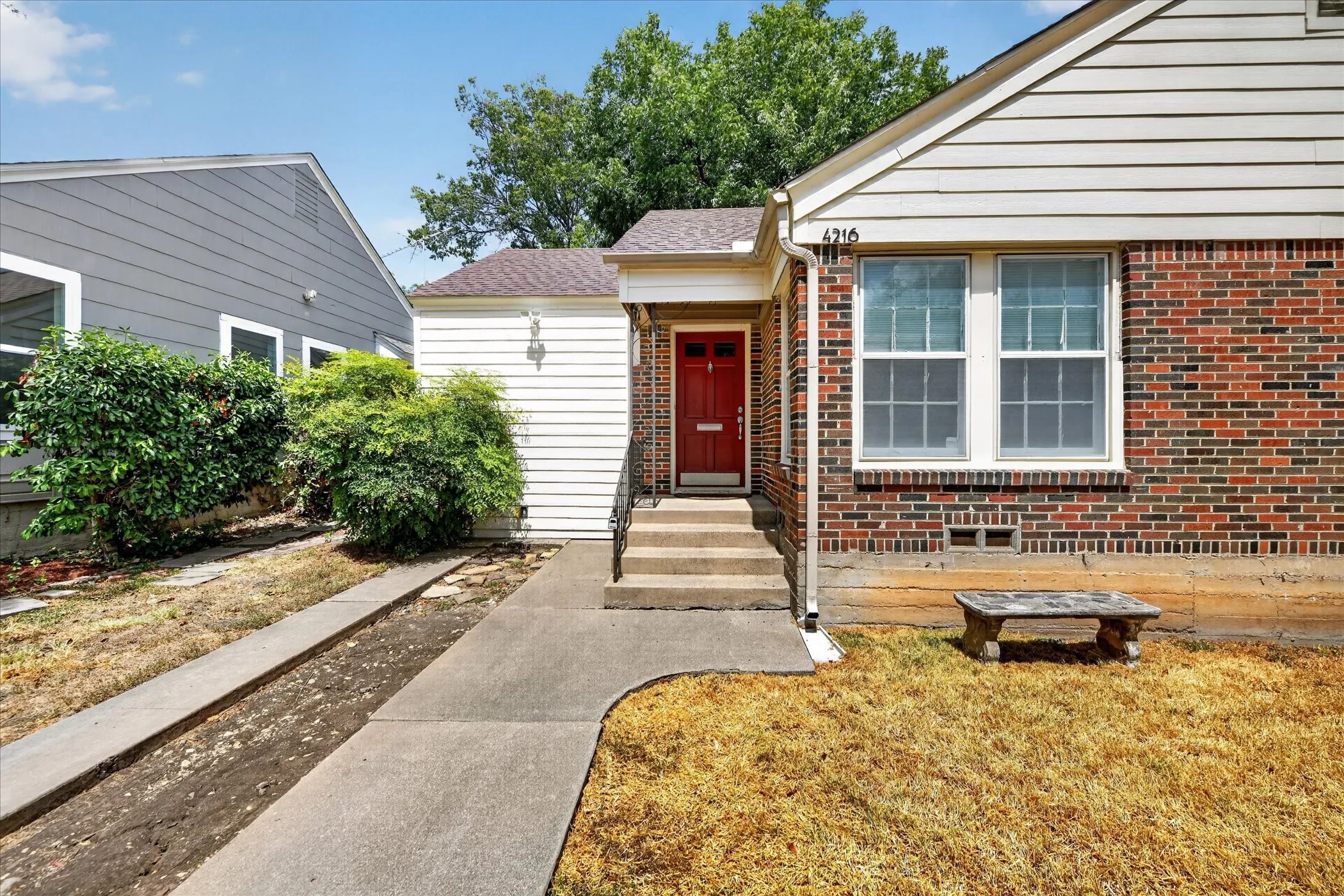 Brick and siding exterior with a red entry door, concrete walkway, and established landscaping