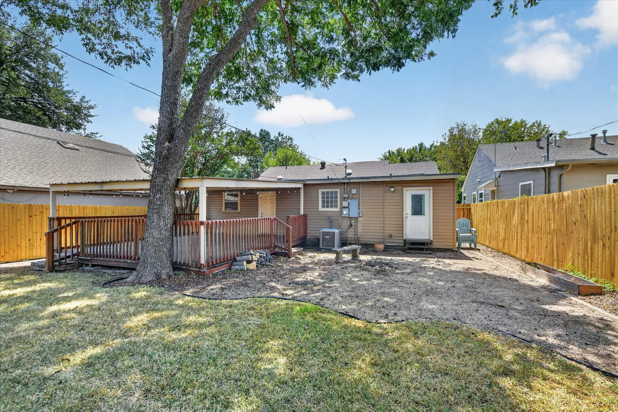 Expansive wooden deck with a covered area, mature tree, and newly installed wooden fence