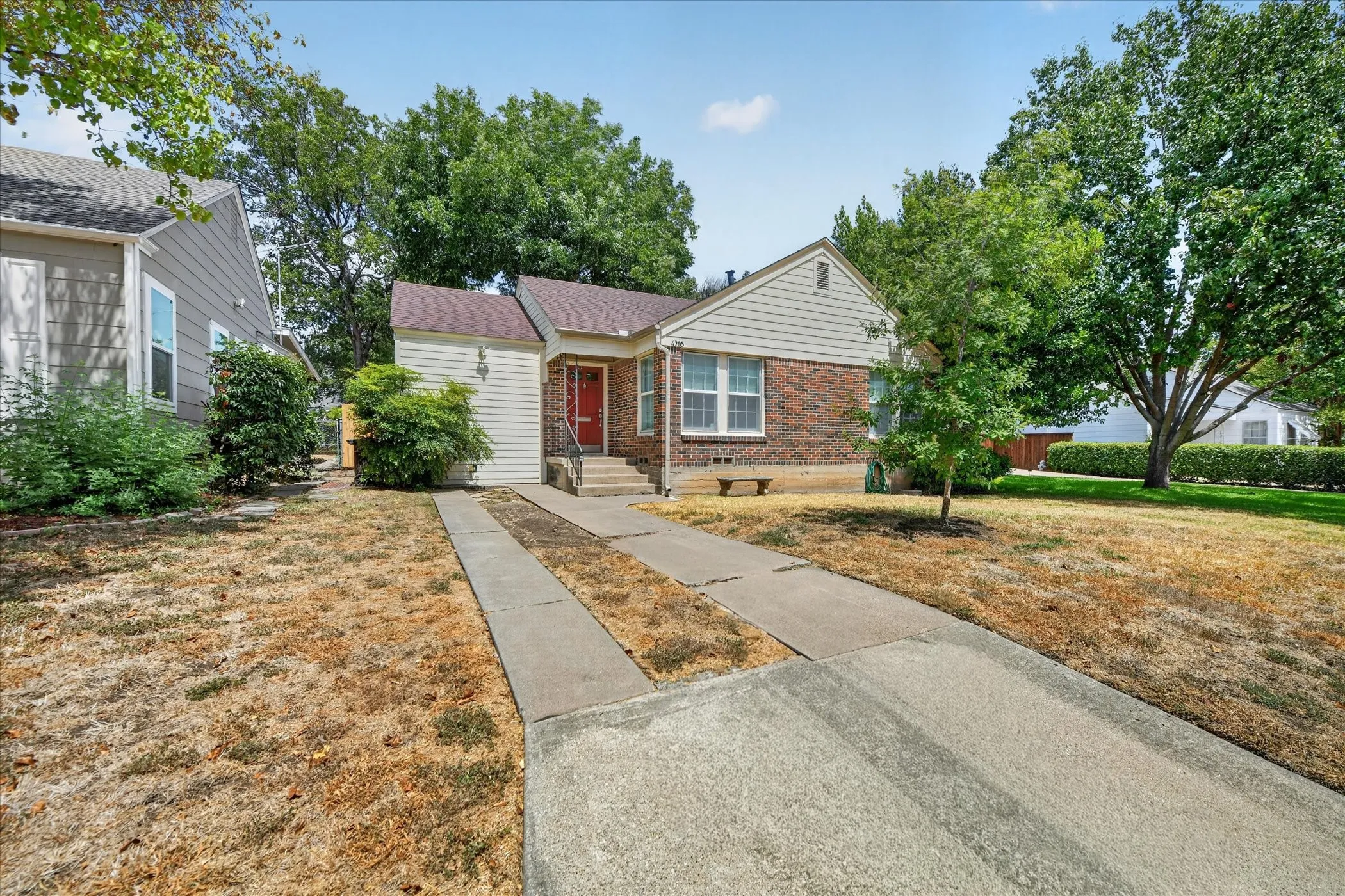 Brick and siding exterior with a red entry door, framed by mature trees, and a concrete driveway