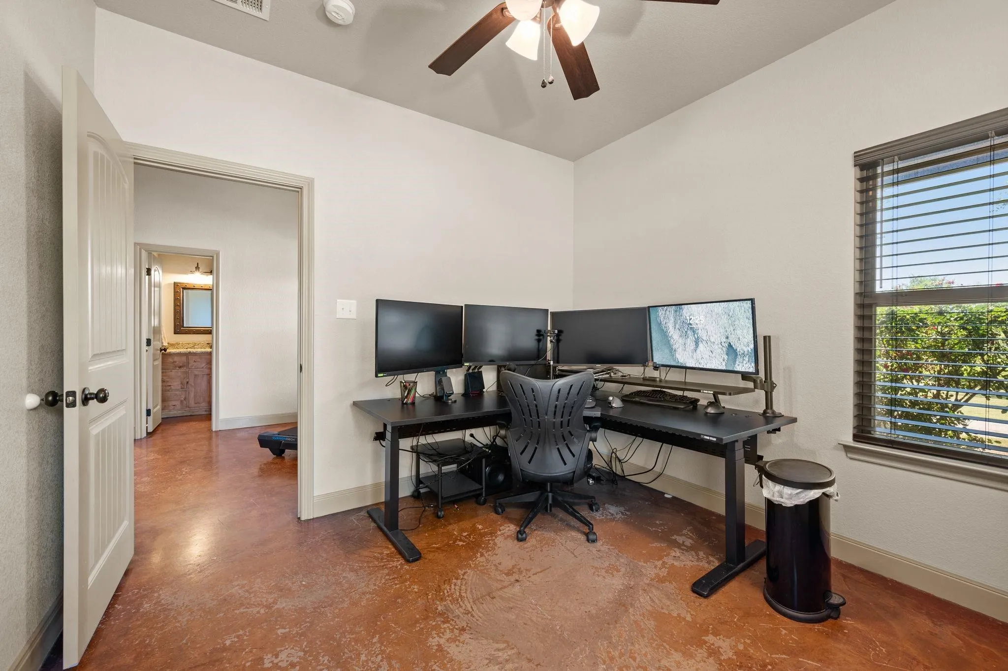 Stained concrete flooring, ceiling fan with integrated lighting, window with blinds, and painted interior doors