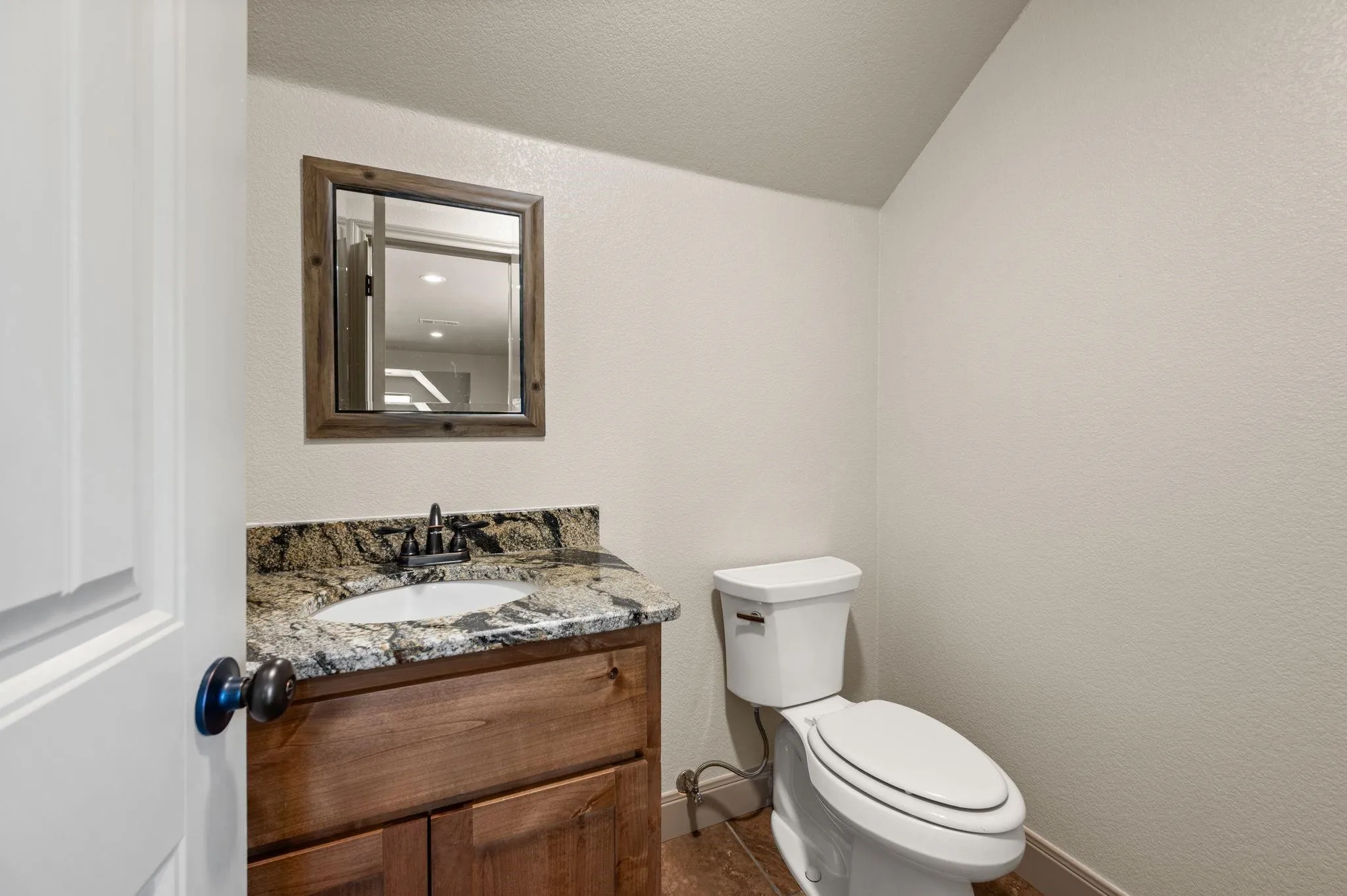 Bathroom featuring a wood-finish vanity with an integrated sink, granite-style countertop, and a wood-framed mirror