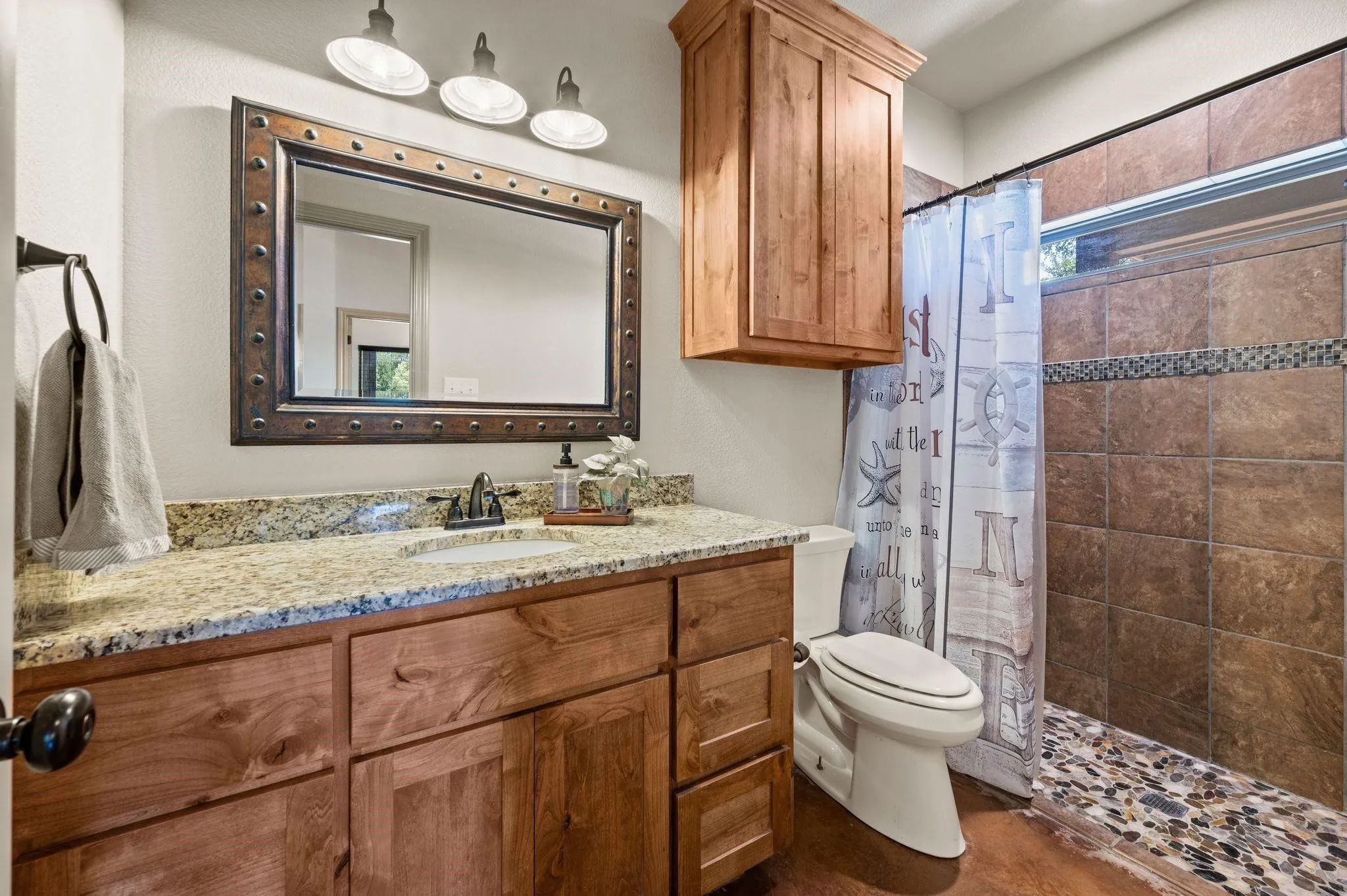 Vanity with a granite countertop, wood-finish cabinetry, and a framed mirror
