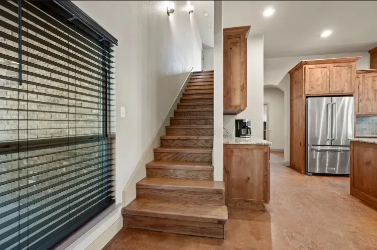 Wood-finish staircase with recessed lighting, wood-finish cabinetry, stainless steel refrigerator, and light-toned countertop