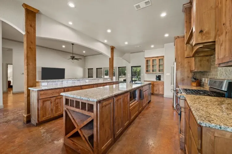 Spacious kitchen featuring two large islands with granite countertops, stainless steel appliances, extensive wood cabinetry, and a tile backsplash