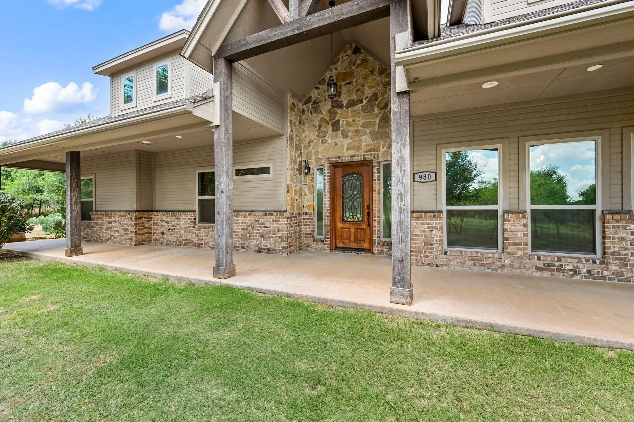 Stone and brick exterior with a covered porch, wood columns, and a paneled entry door with decorative glass