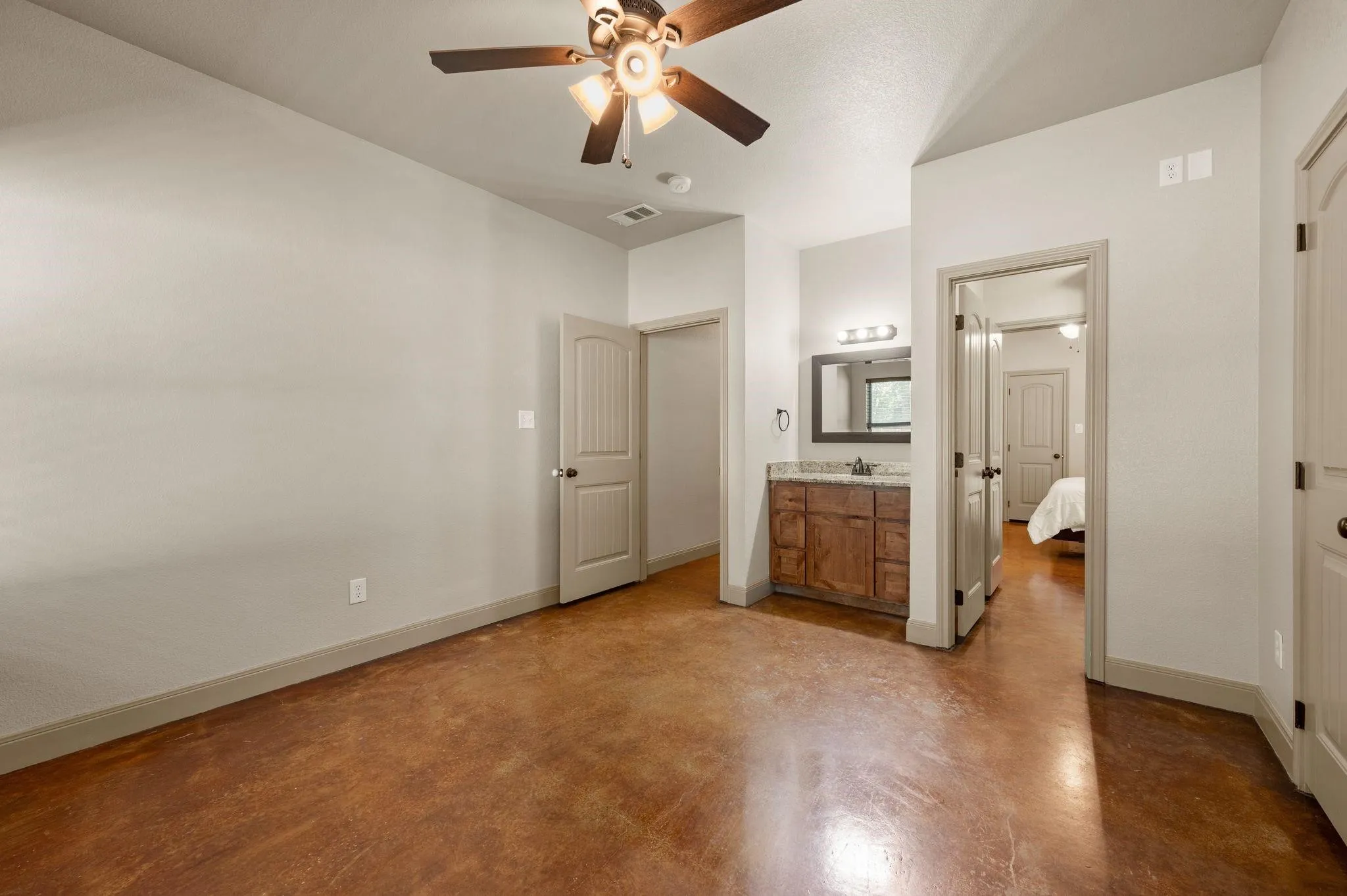 Stained concrete flooring, ceiling fan with integrated lighting, wood-finish vanity with stone countertop, mounted mirror, and vanity lighting
