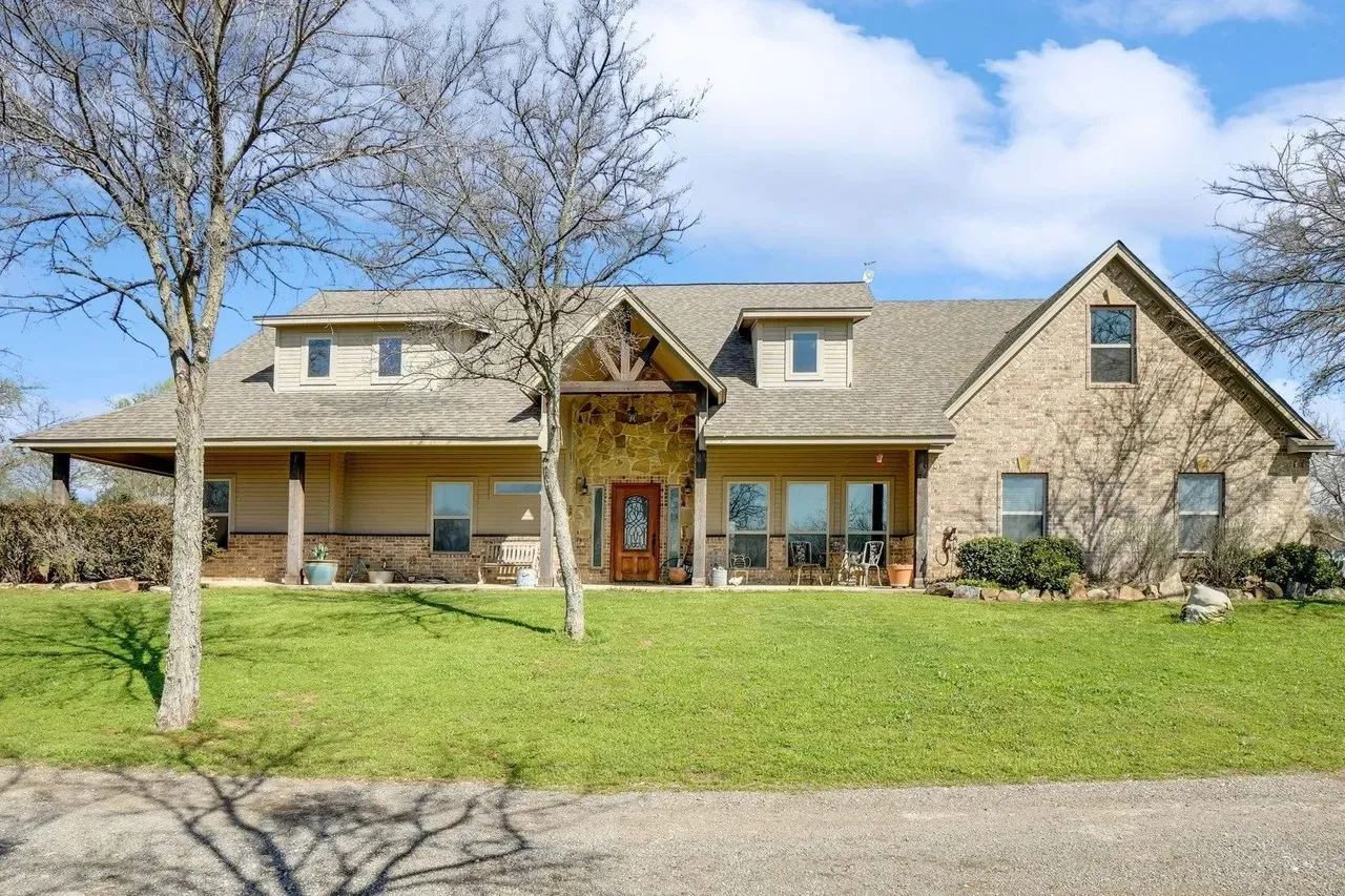 Expansive front lawn with mature trees, a covered porch, and a brick and stone exterior