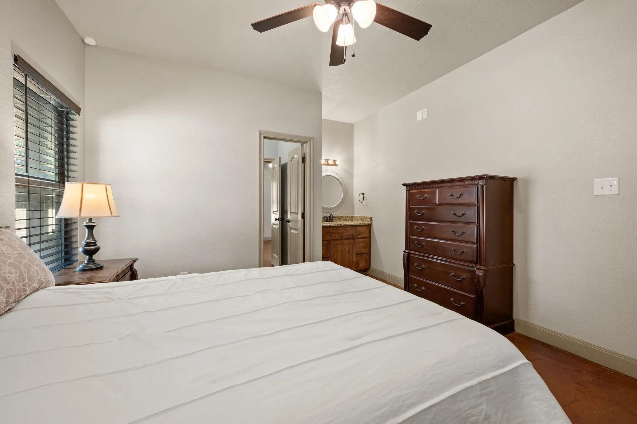 Vaulted ceiling with a ceiling fan, window with blinds, wood-finish flooring, and an attached bathroom featuring a vanity with an undermount sink and a round mirror