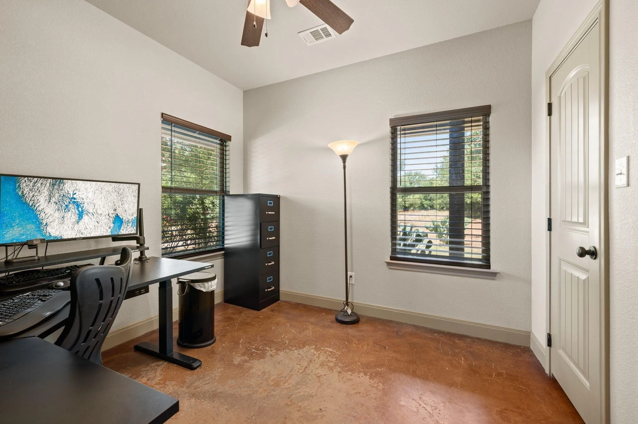Neutral wall paint, ceiling fan, two windows with blinds, light-toned flooring, and a paneled door