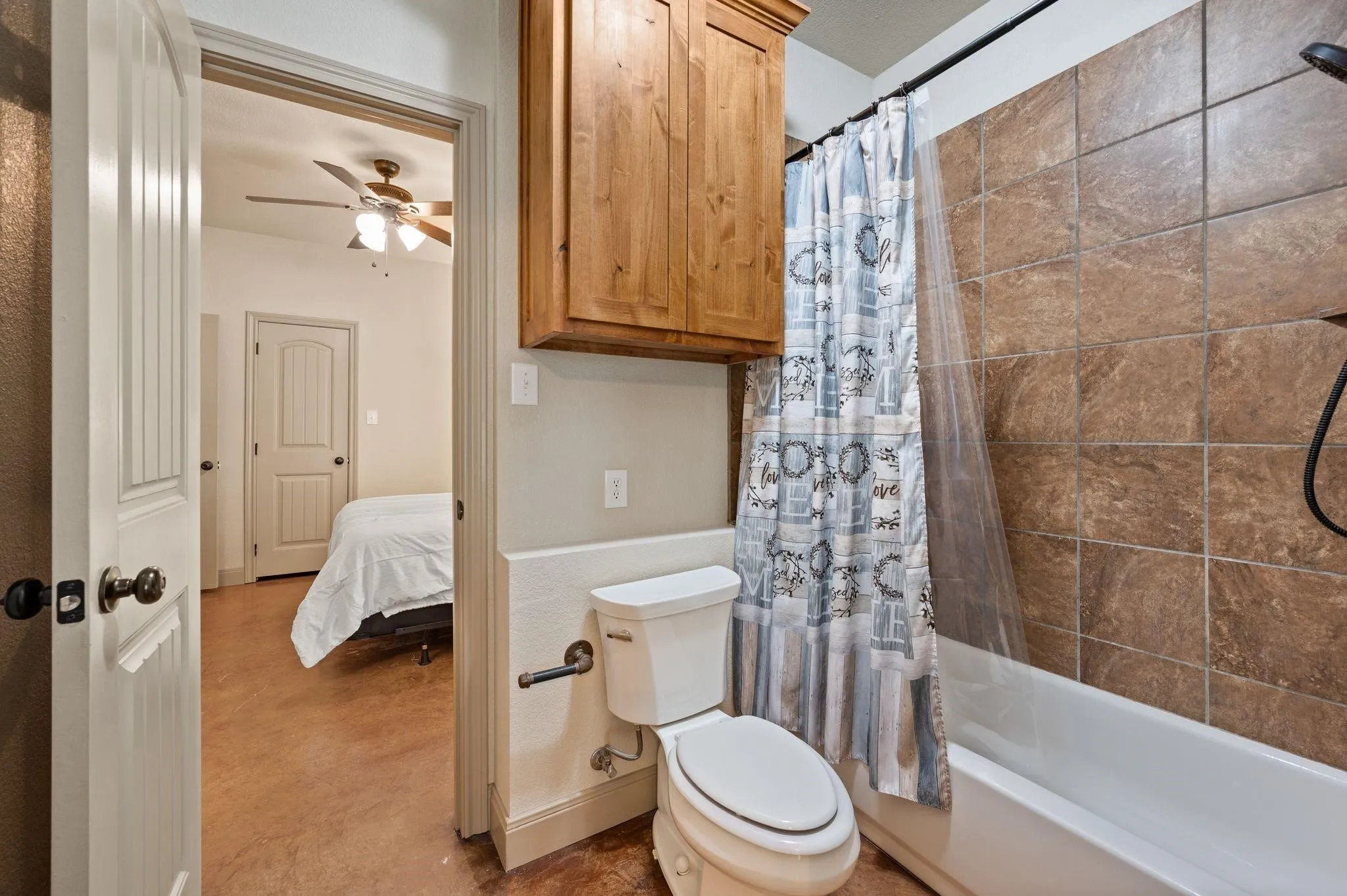 Full-size bathtub with tiled shower surround, built-in wooden cabinetry, and a standard toilet