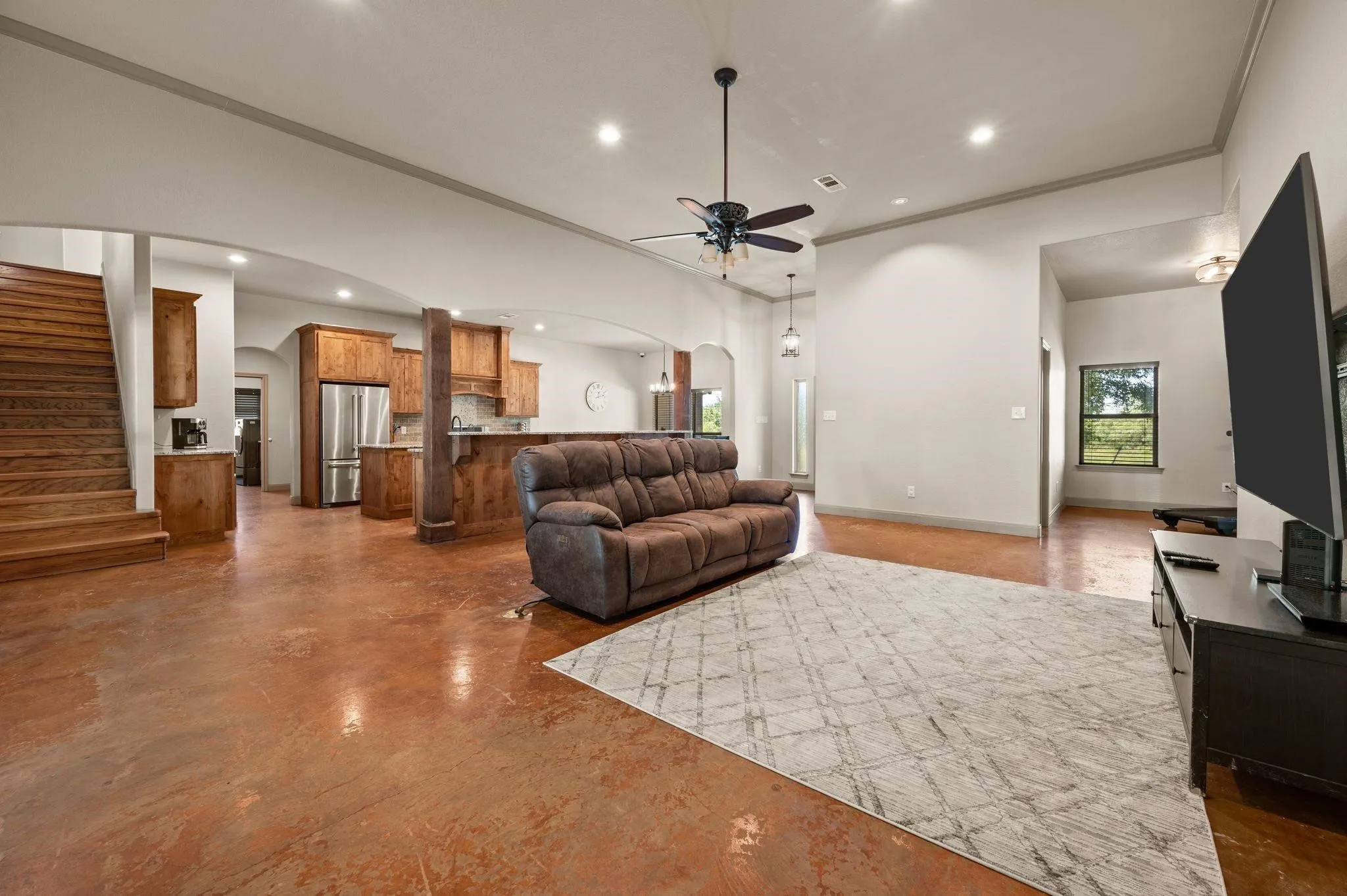 Open-concept living area featuring stained concrete flooring, recessed lighting, ceiling fan, and wood staircase