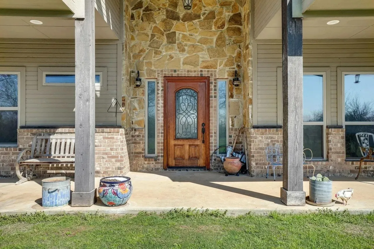 Stone and brick facade with a wood-finish entry door, sidelight windows, and a covered porch with structural columns
