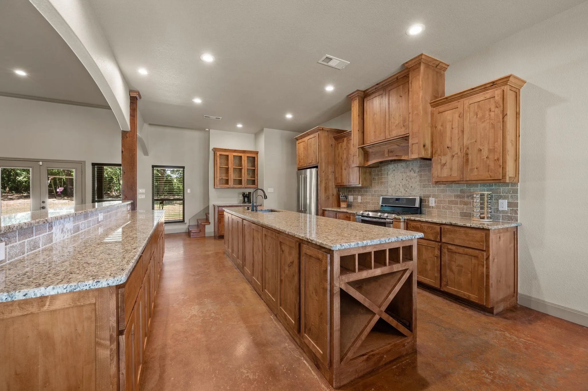 Spacious kitchen featuring an expansive island, light wood-finish cabinetry, light granite countertops, a tiled backsplash, and recessed lighting