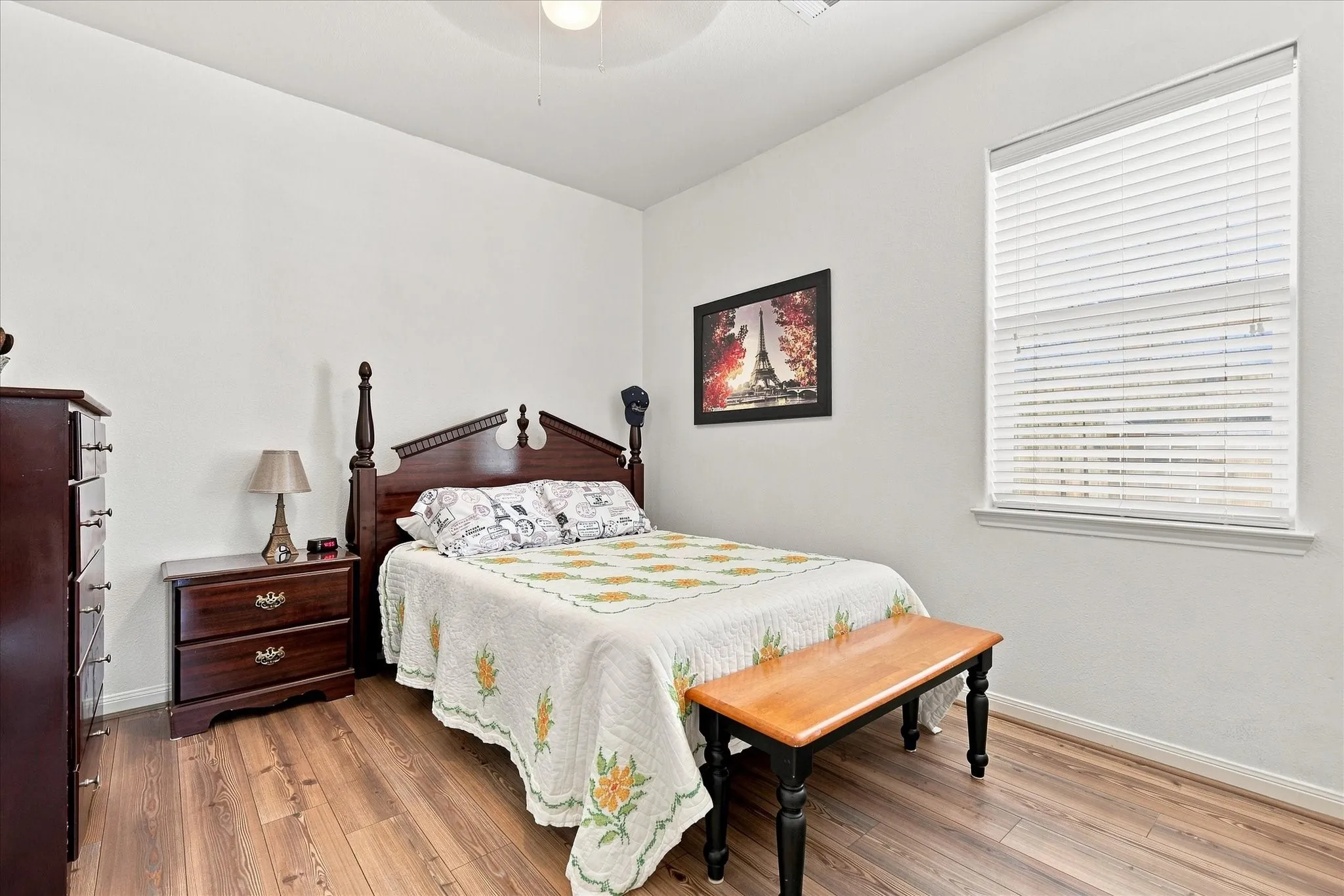 One of the two secondary bedrooms, complete with wood-finish flooring, tall double doors, clean white walls, and bright windows with built-in blinds.
