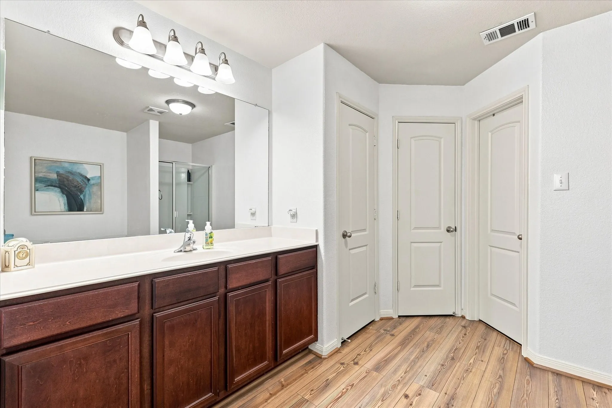 The primary bathroom suite coordinates beautifully with the new wood-finish LPV flooring flowing into the space. Features include an expansive vanity, large mirror, and separate walk-in shower