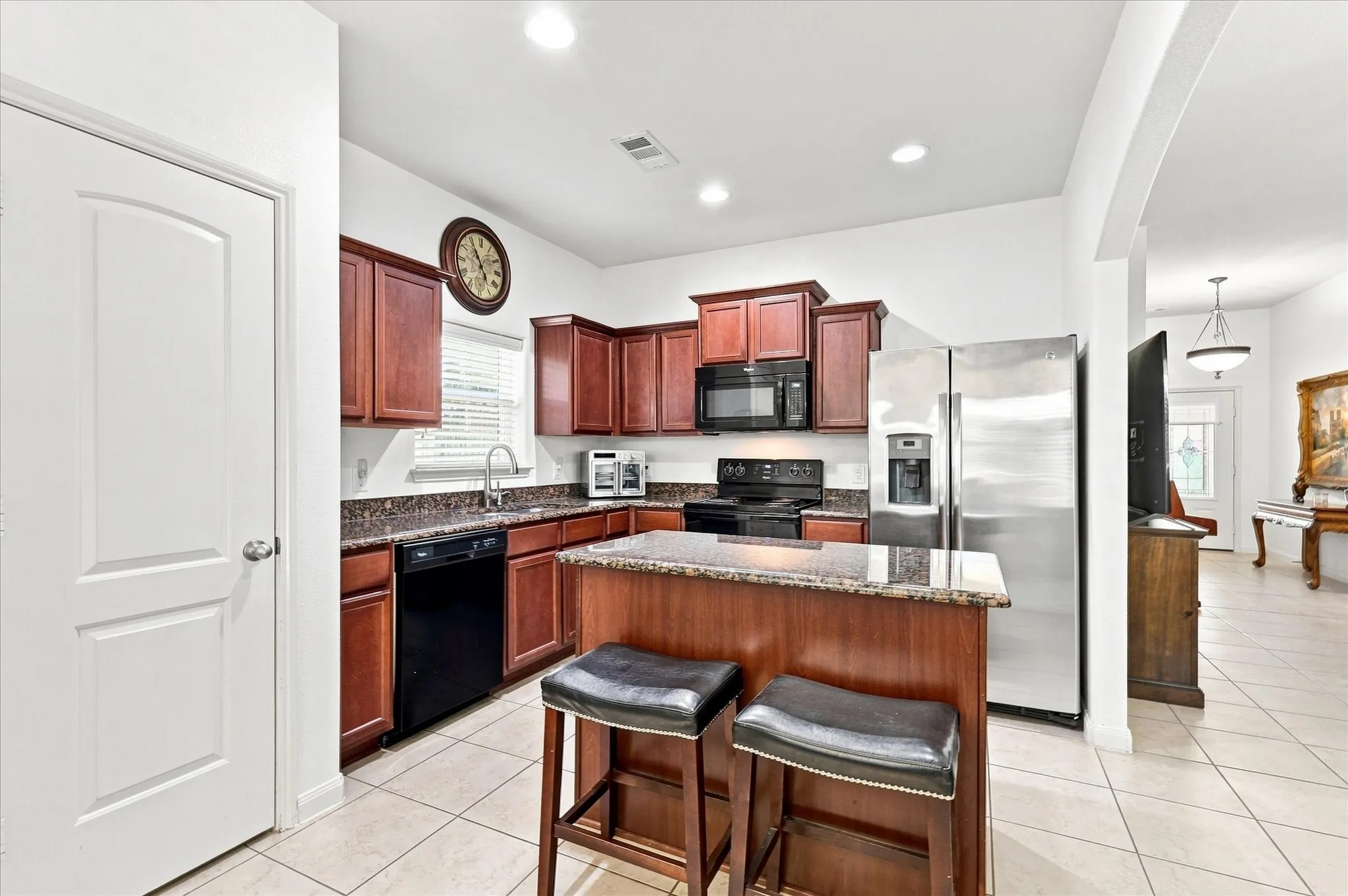Kitchen featuring wood cabinetry, stainless steel refrigerator, black appliances, a stone countertop, and tile flooring