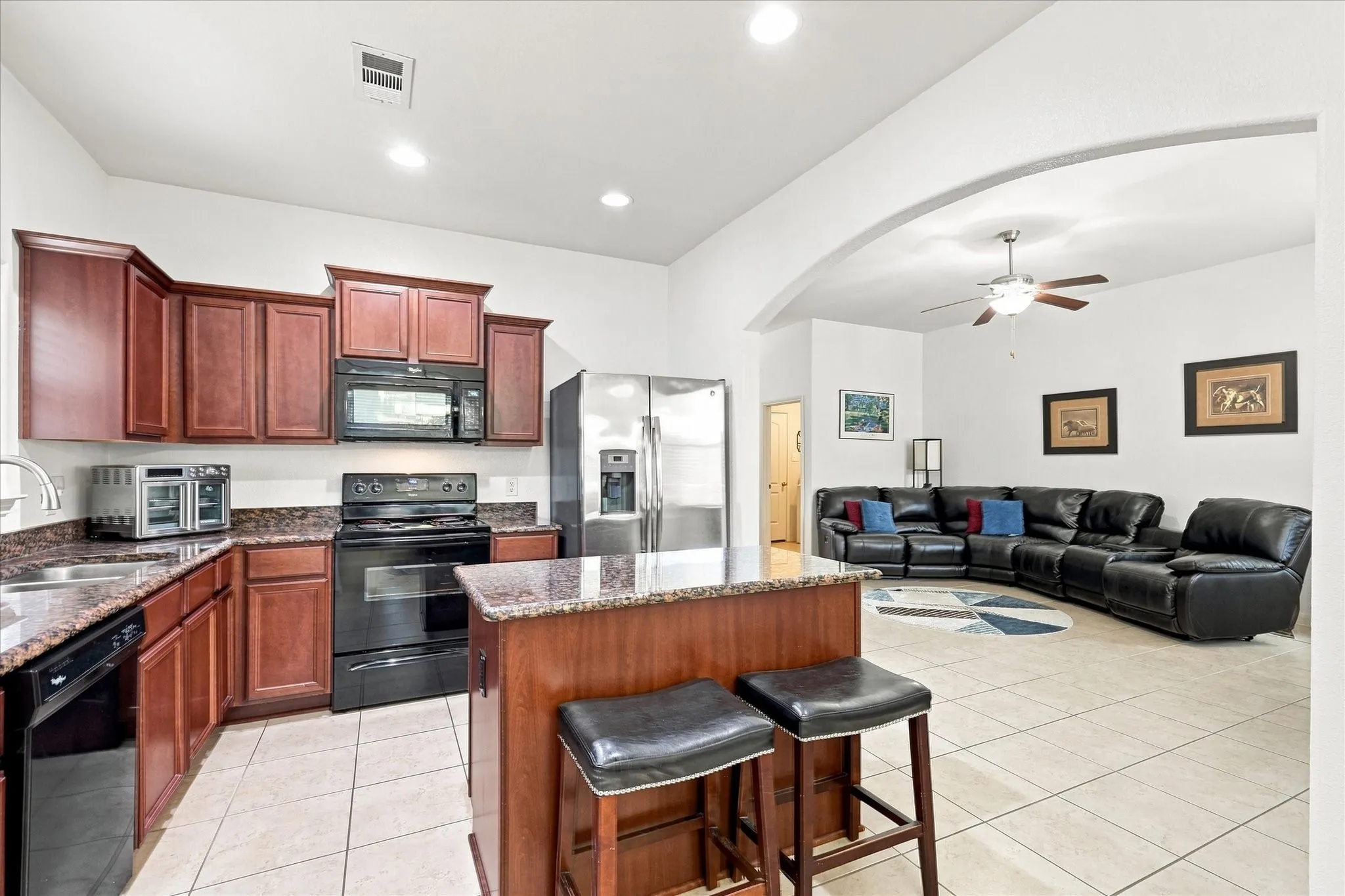 A clean, functional kitchen featuring rich wood cabinetry, stainless steel appliances, and a central island. It opens directly to the living and dining spaces, keeping the entire home connected.