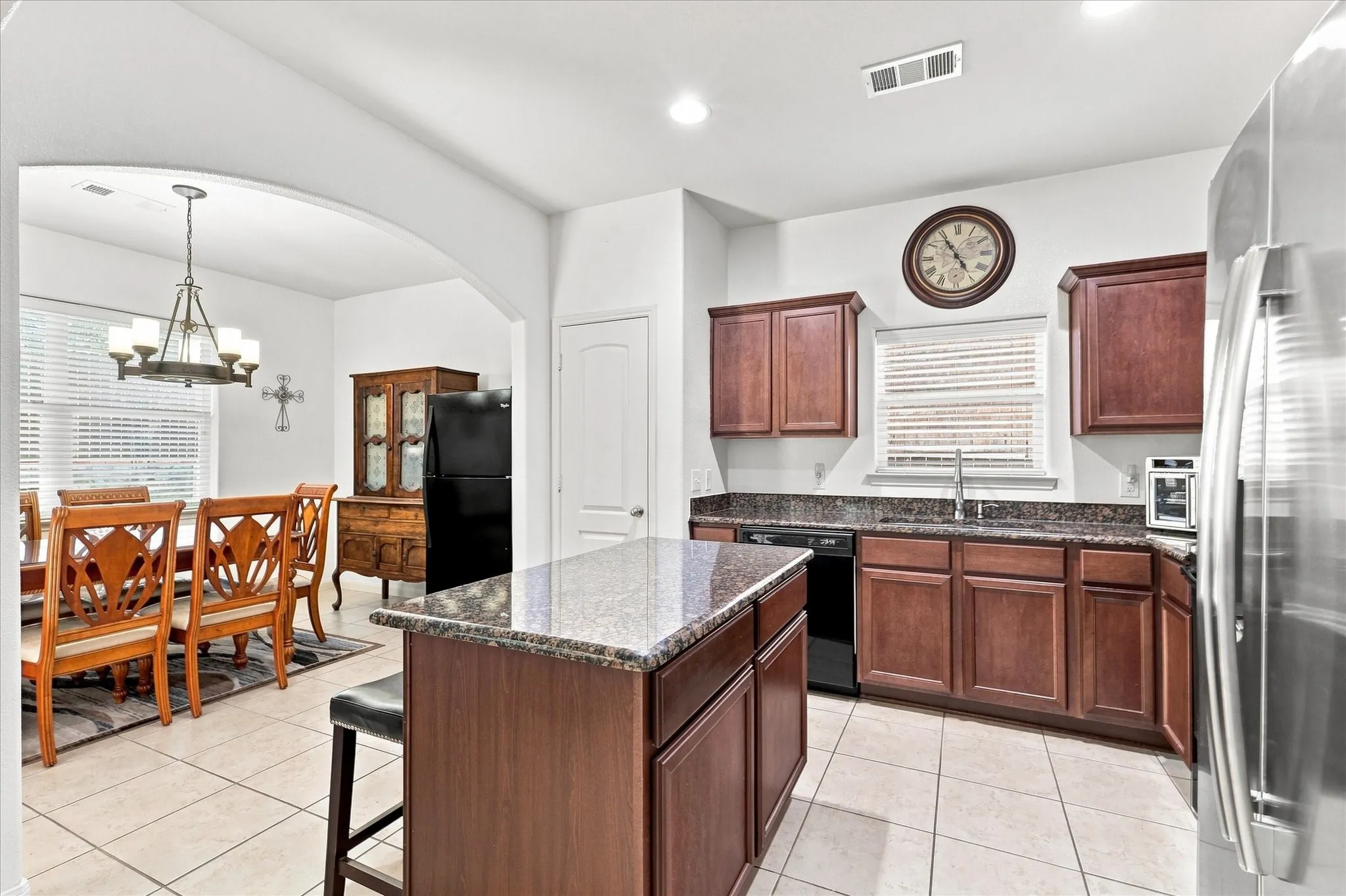 The dedicated dining space accommodates a large table and features a classic chandelier. Large windows with horizontal blinds let in plenty of natural light