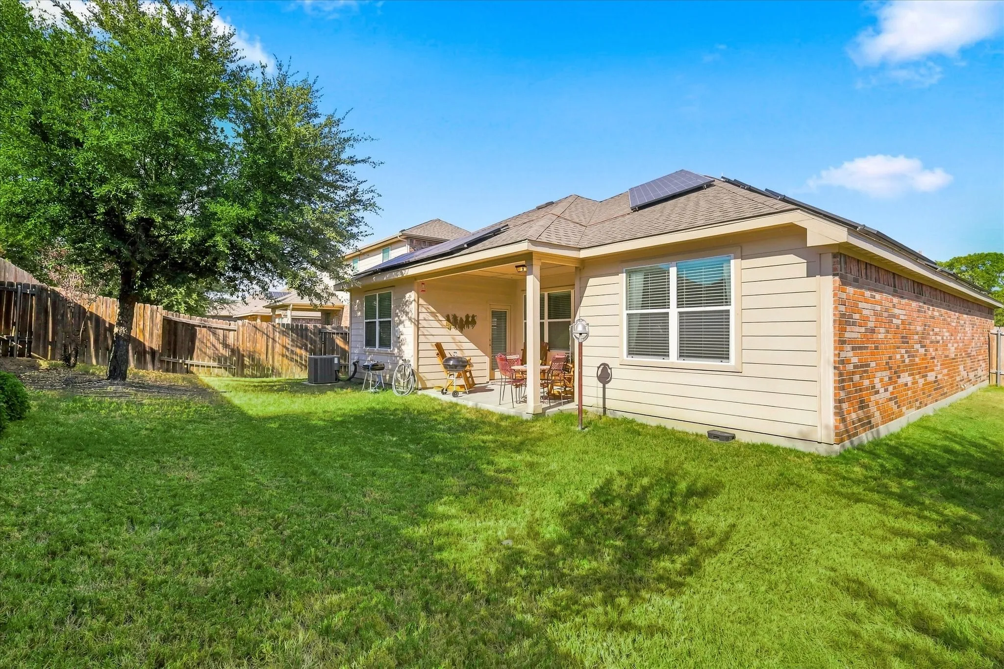 Expansive backyard featuring a covered patio, wood fencing, and solar panels