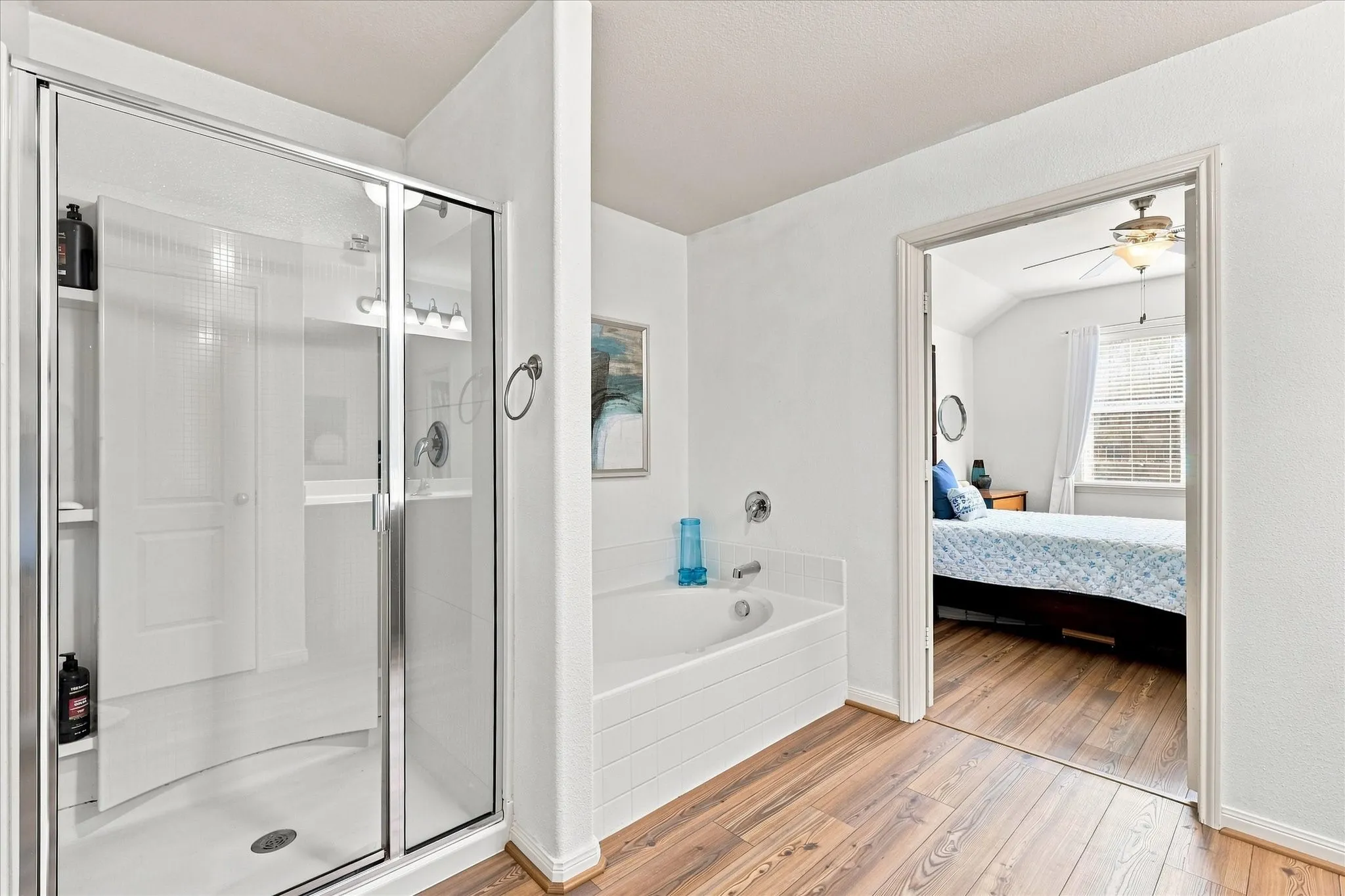 Separate Shower with clear glass enclosure and built-in shelving, white bathtub, and wood-finish flooring. Tall ceilings and double vanity.