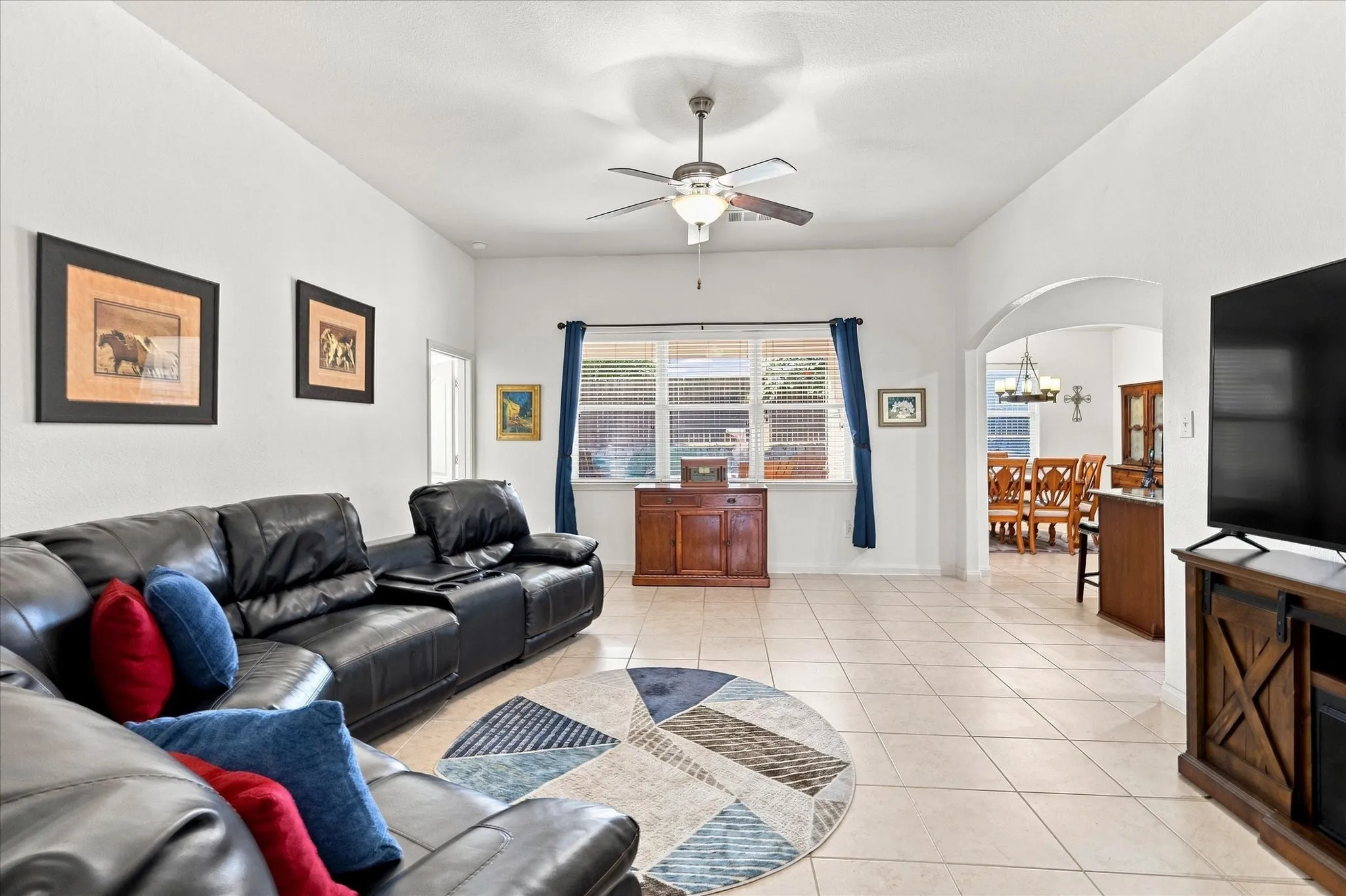 The expansive living room boasts tall ceilings and a modern ceiling fan, creating a bright and airy atmosphere. The open-concept design flows seamlessly into the kitchen, ideal for entertaining family and guests.
