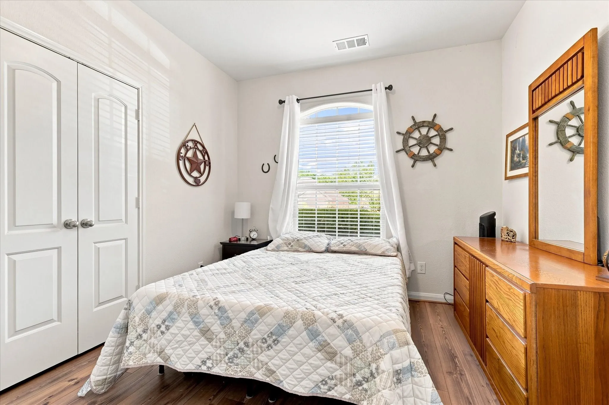 Wood-finish flooring, white double doors with arched panels, arched window with blinds, and white walls