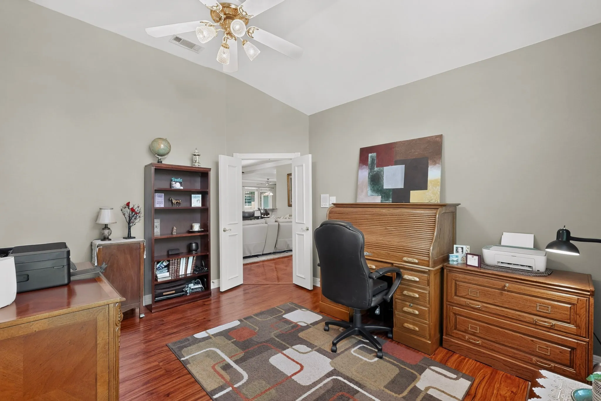 Vaulted ceiling with a ceiling fan, wood-finish flooring, and light gray wall paint