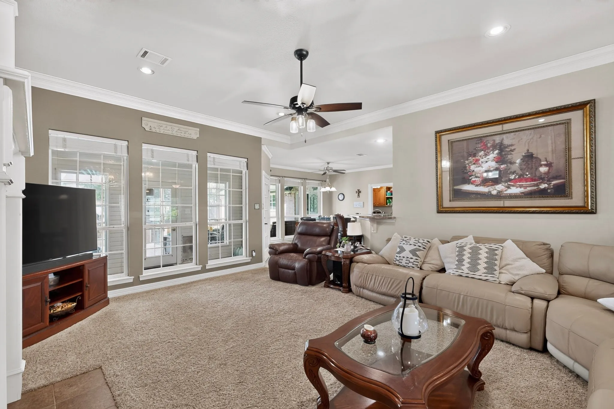 Tray ceiling with a ceiling fan, recessed lighting, crown molding, and large grid-pattern windows
