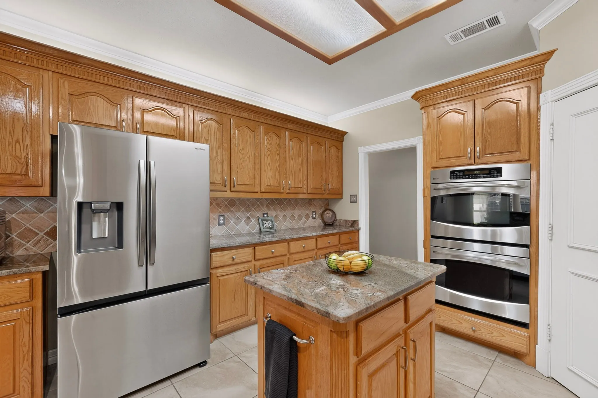 Kitchen featuring wood cabinetry, stainless steel appliances, a tiled backsplash, a central island with a stone-finish countertop, and crown molding