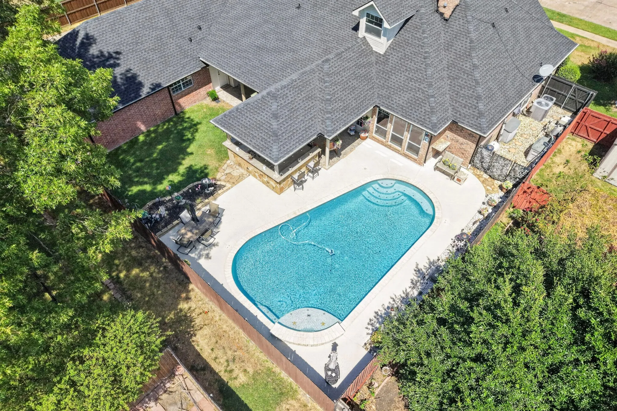 Oval-shaped inground pool with integrated steps, surrounded by a light-colored concrete patio
