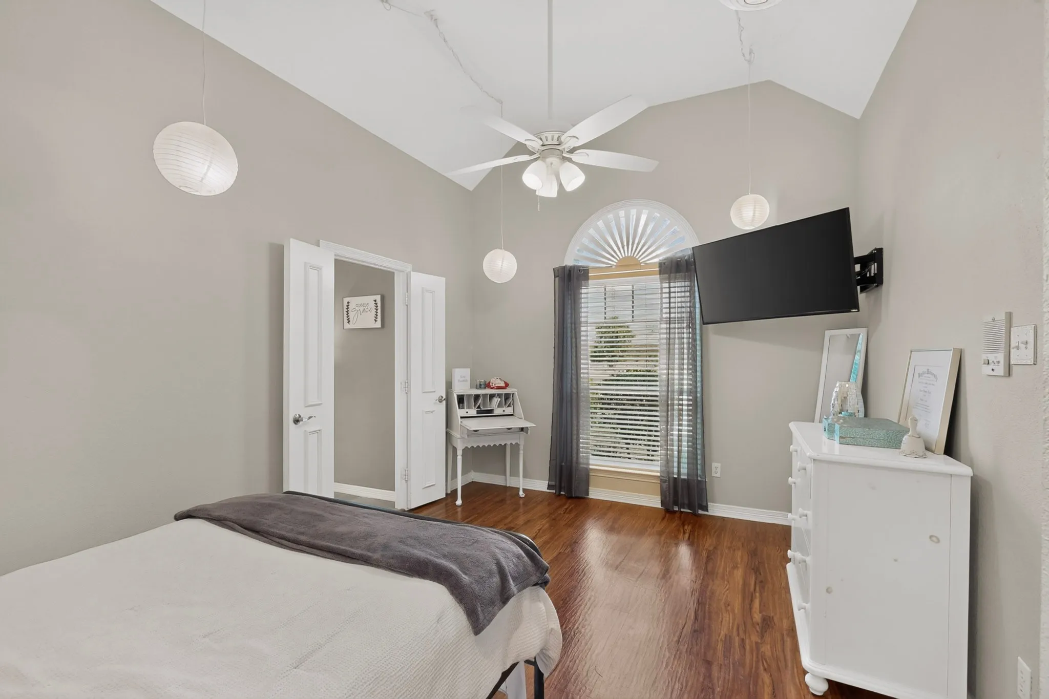 Vaulted ceiling, wood-finish flooring, arched window, ceiling fan, and double bi-fold doors