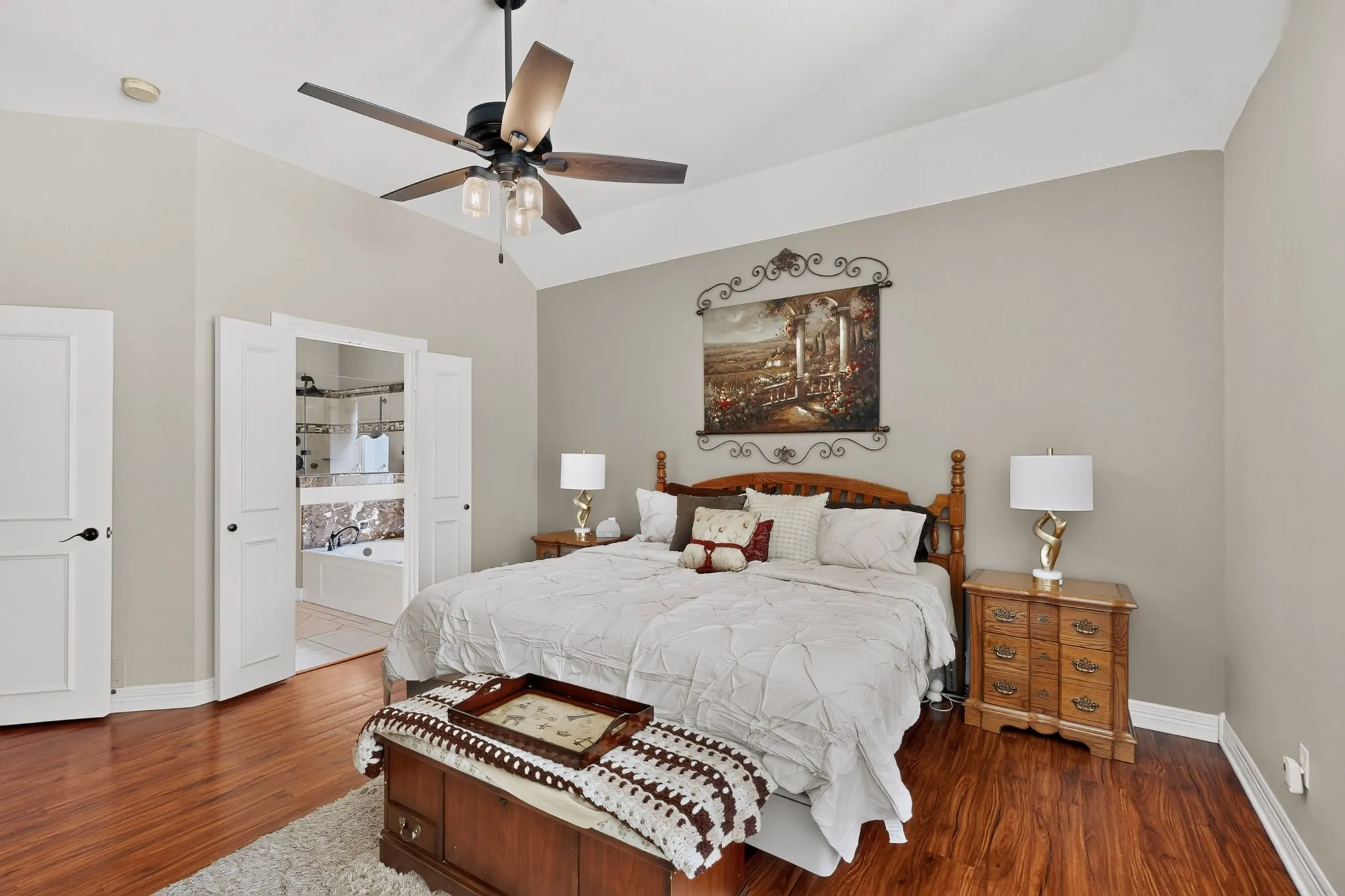 Vaulted ceiling with a ceiling fan, wood-finish flooring, two-panel interior doors, and a built-in bathtub with tiled surround