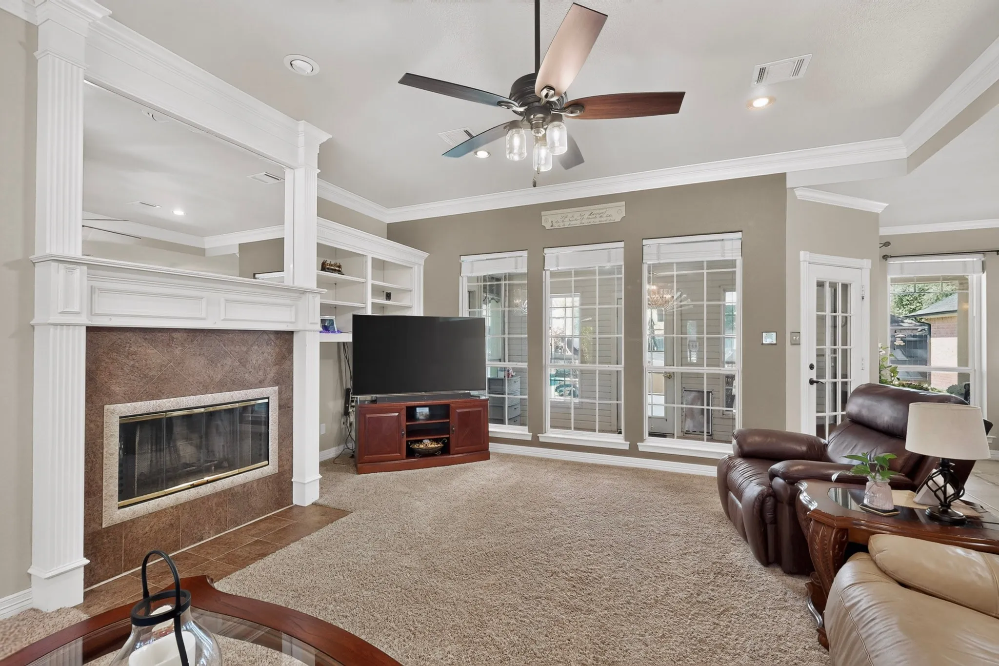 Carpeted living area featuring a built-in fireplace with a hearth, multiple windows, a ceiling fan, and crown molding