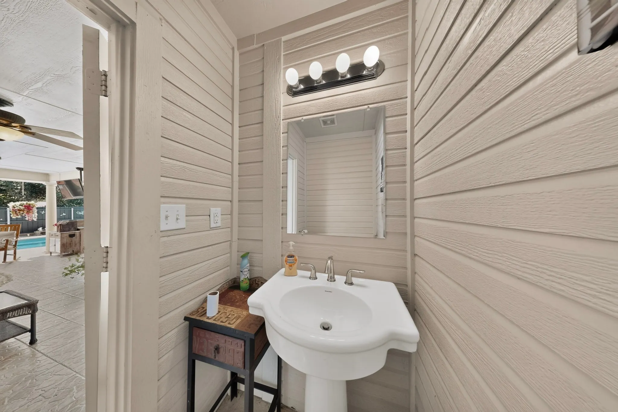 Pedestal sink with chrome fixtures, framed mirror, and a vanity light bar