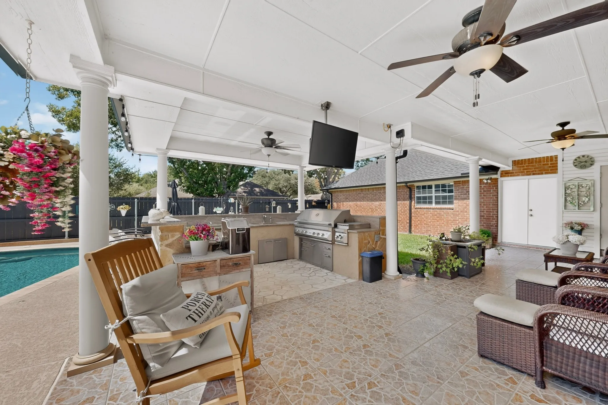 Covered outdoor patio featuring a built-in outdoor kitchen, ceiling fans, and a mounted screen
