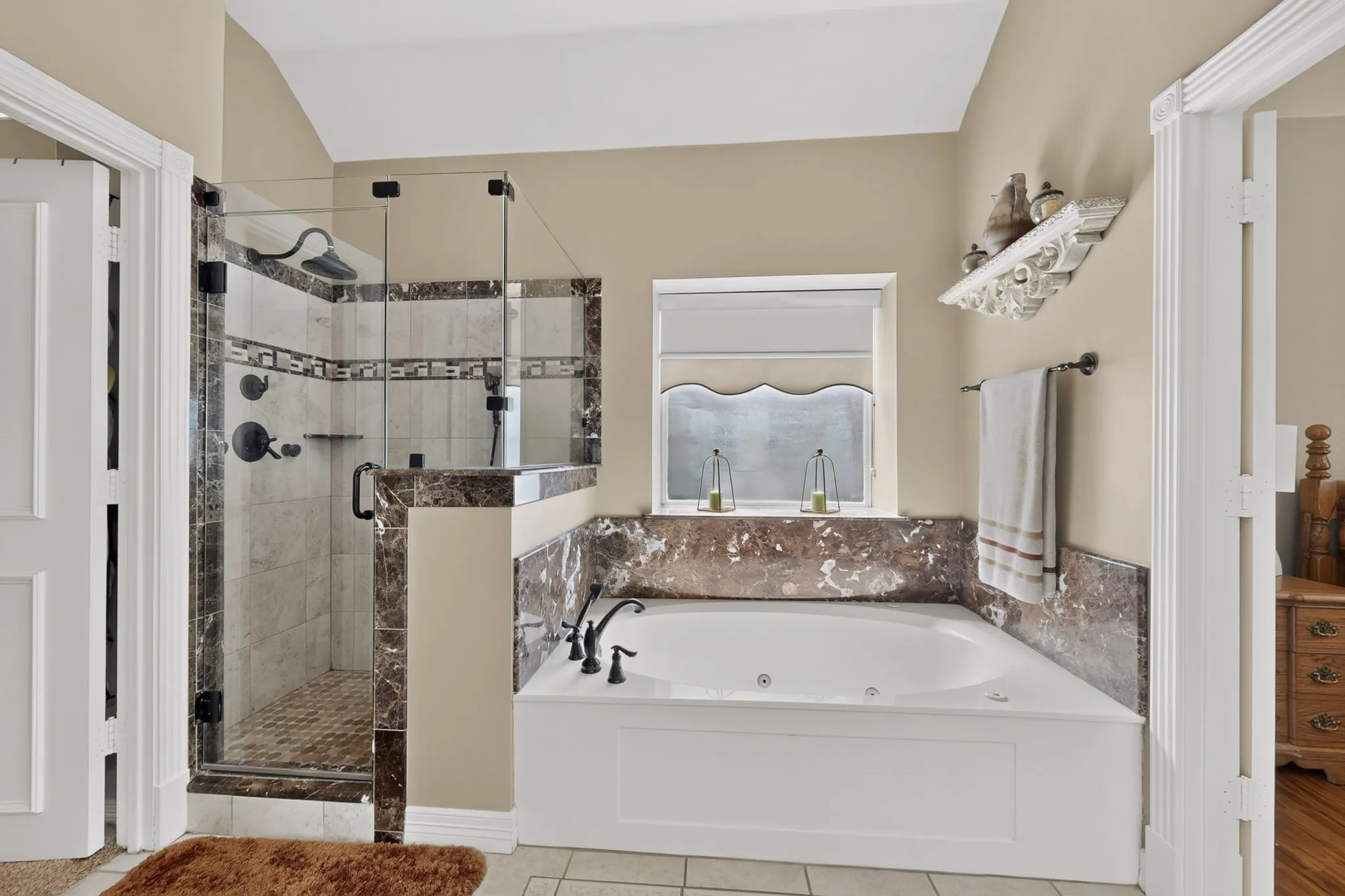 Glass-enclosed shower with dark-toned tile accents, an integrated soaking tub, and a window with a roller shade