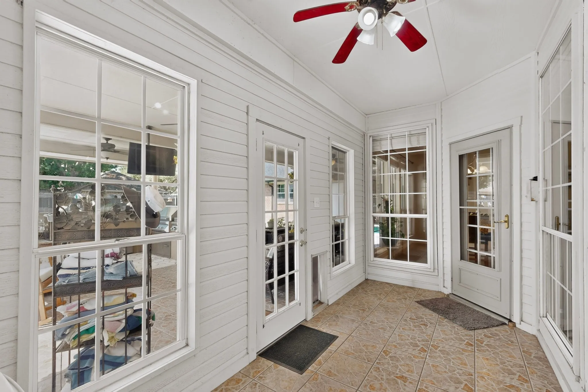 Enclosed patio with tile flooring, white plank walls, multiple large windows, a ceiling fan, and French doors