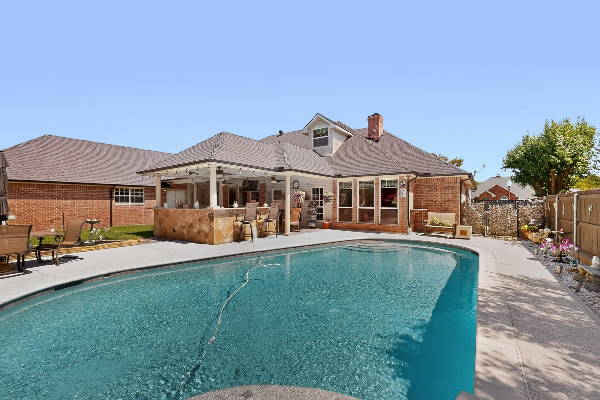 Backyard oasis featuring a large swimming pool, expansive concrete patio, and a covered outdoor kitchen with a stone-clad bar