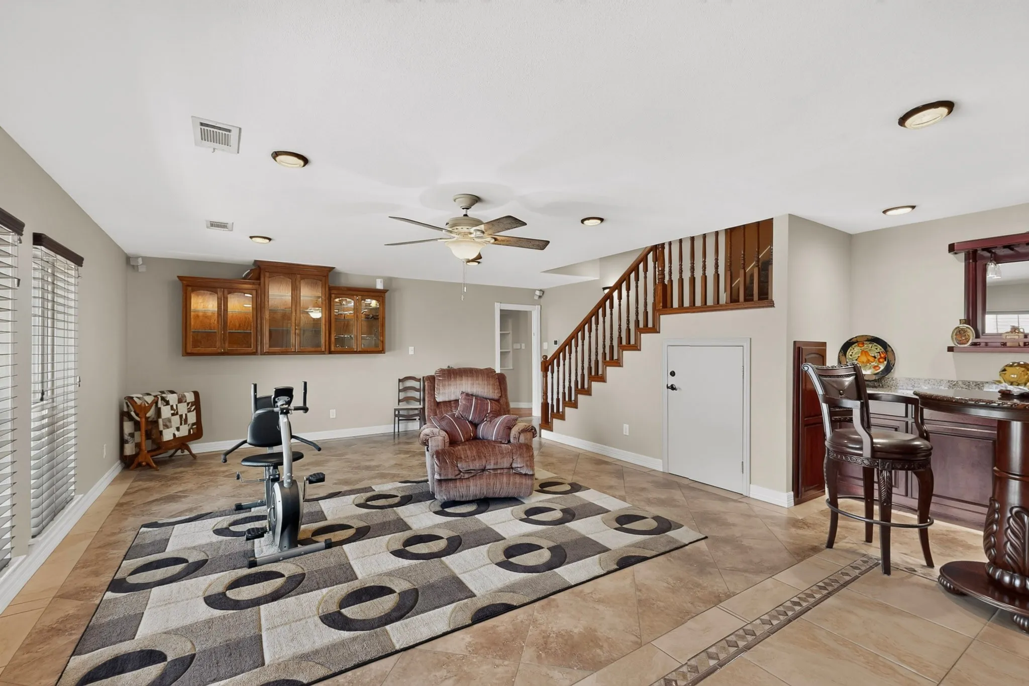 Spacious room featuring tile flooring, a wood-finish staircase with balusters, built-in wood-finish cabinetry, and recessed lighting