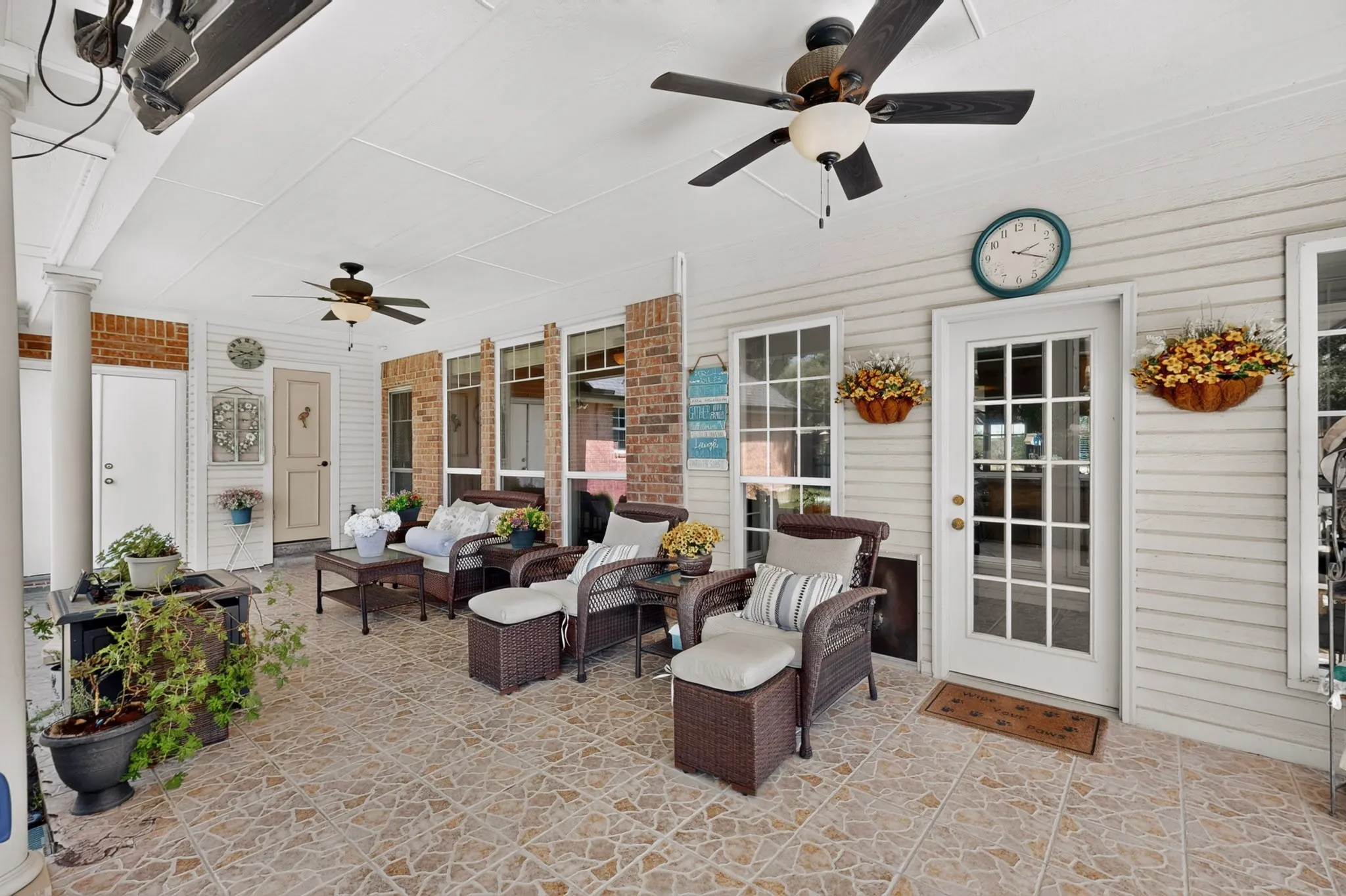Covered porch with tile flooring, white siding, brick accents, and multiple ceiling fans