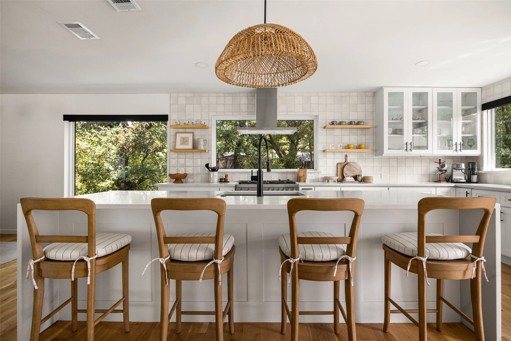 Kitchen featuring white cabinetry, light-toned backsplash tiling, a built-in range hood, and a woven pendant light fixture