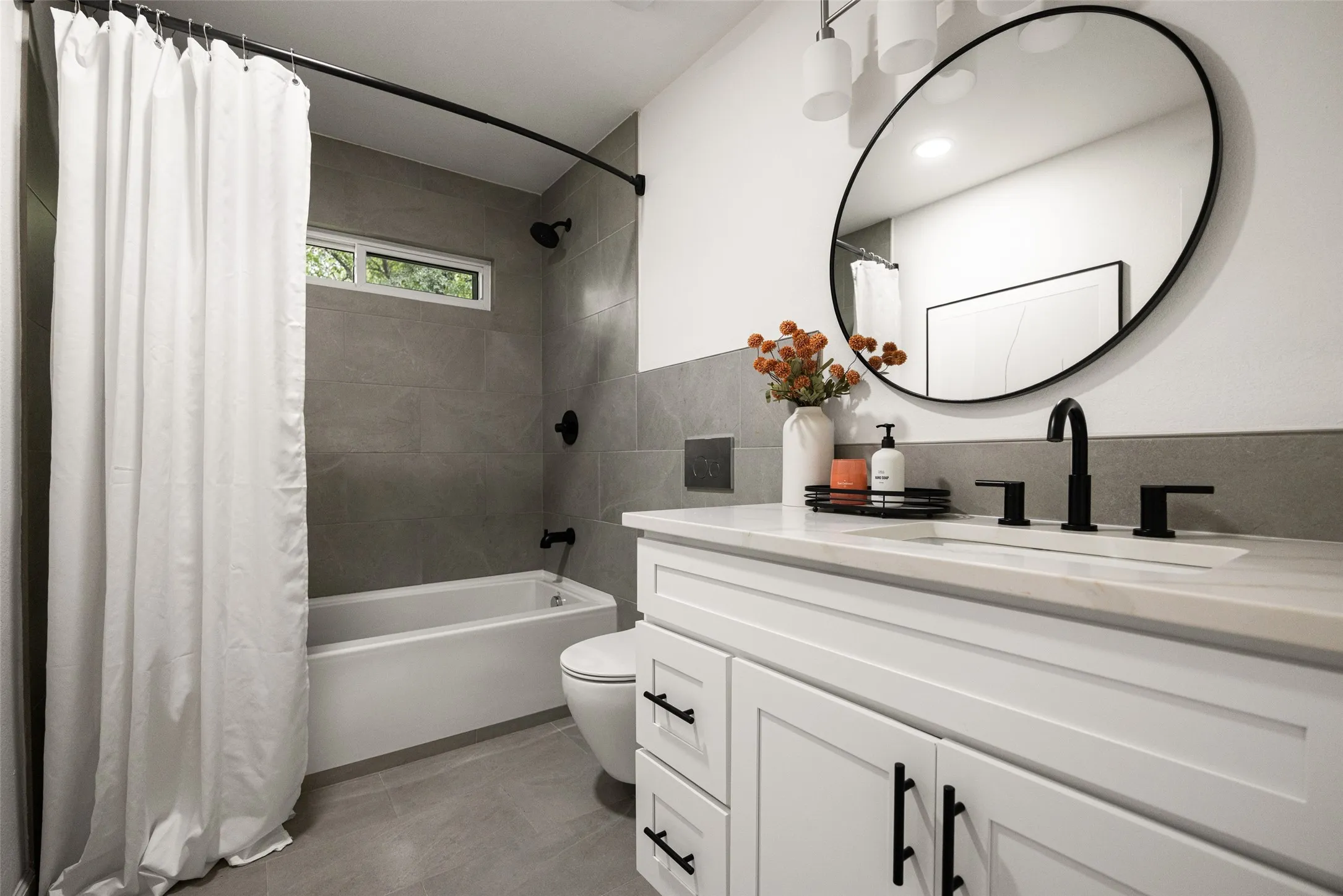 Bathroom featuring a white vanity with shaker-style cabinetry, matte black hardware, a rectangular undermount sink, and a light-toned countertop