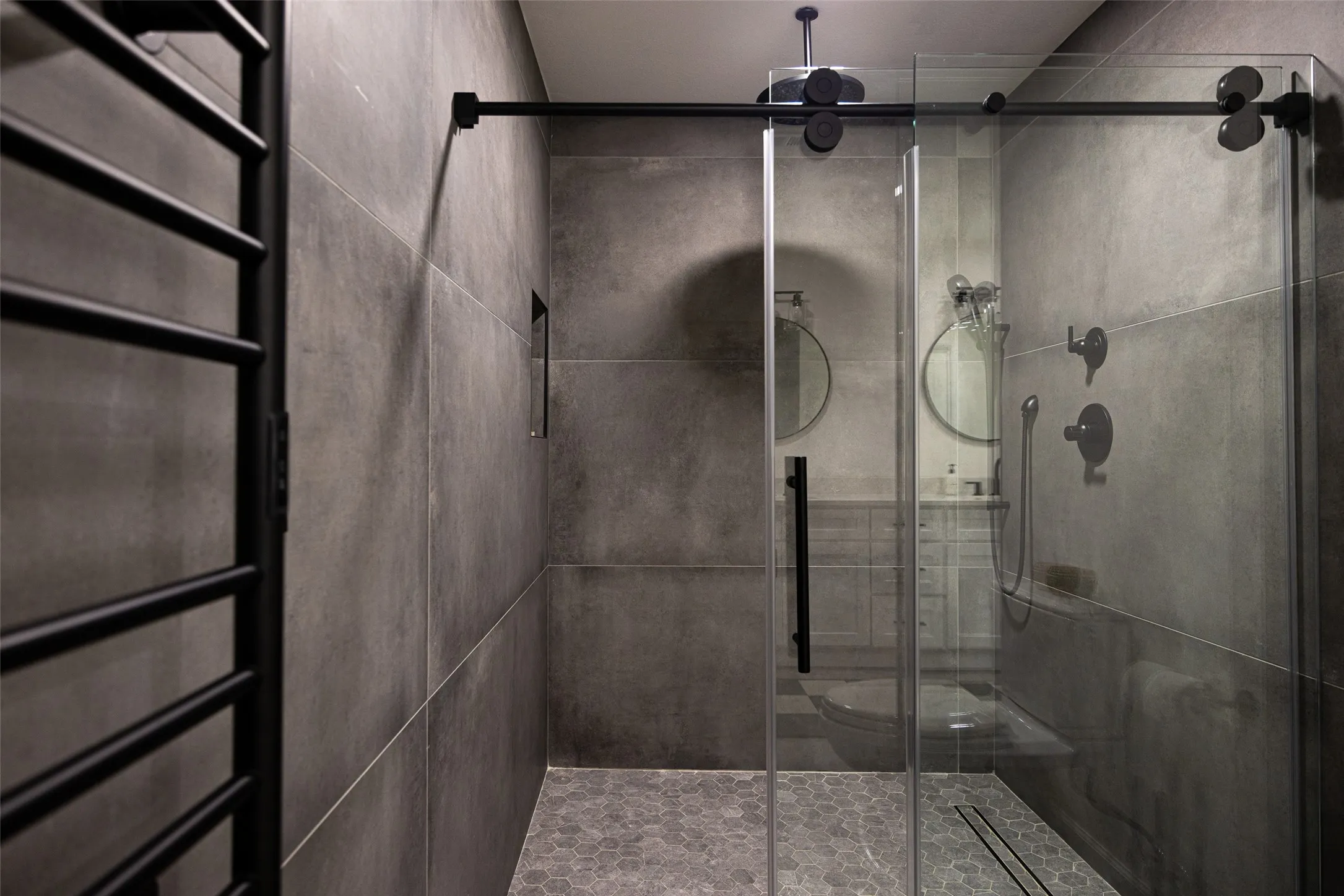 Shower enclosure with sliding glass door, matte black fixtures, full-height wall tiling, and hexagonal floor tiling