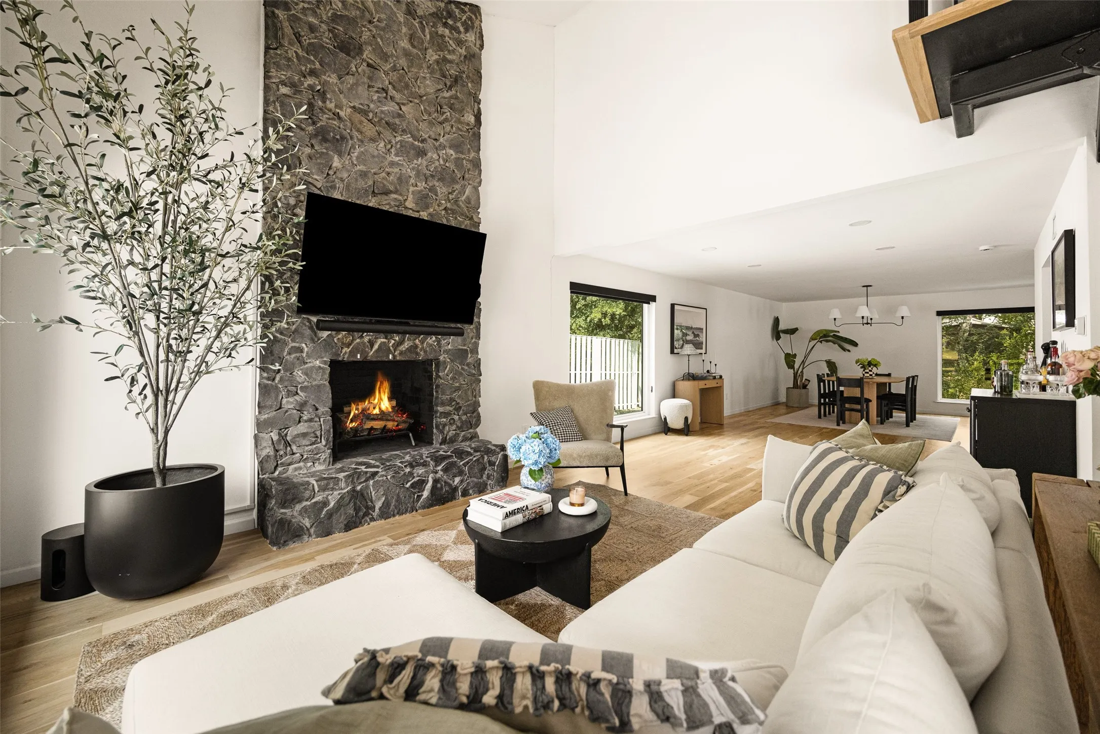 Vaulted ceilings with recessed lighting, stone-finish fireplace, wood-finish flooring, and large windows