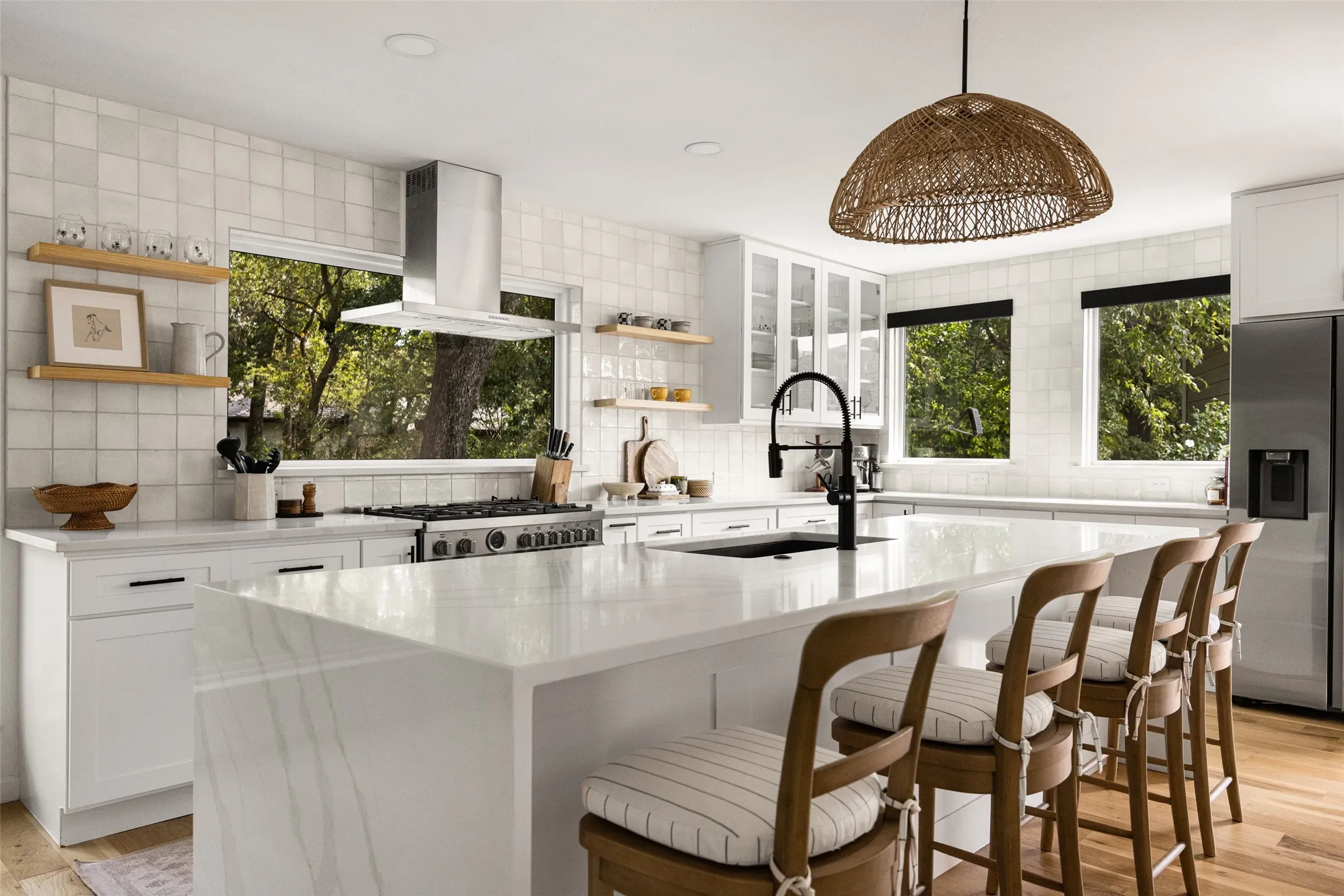 Sleek kitchen featuring white cabinetry, a large center island with a waterfall edge, stainless steel appliances, and a tile backsplash