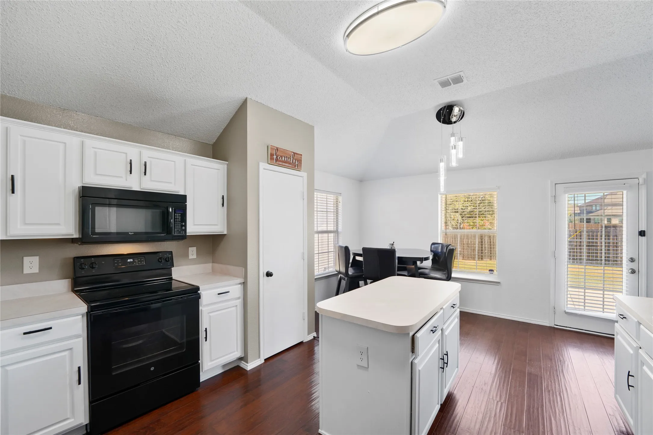 Kitchen featuring wood-finish flooring, white cabinetry, black appliances, a central island, and a dining area with exterior access