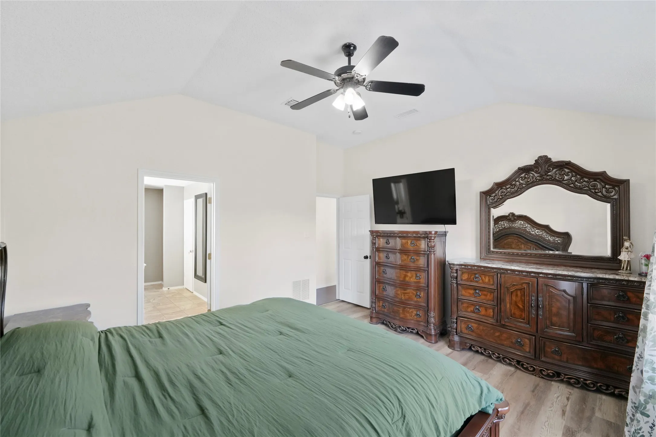 Vaulted ceiling with a ceiling fan, light-toned walls, and wood-finish flooring